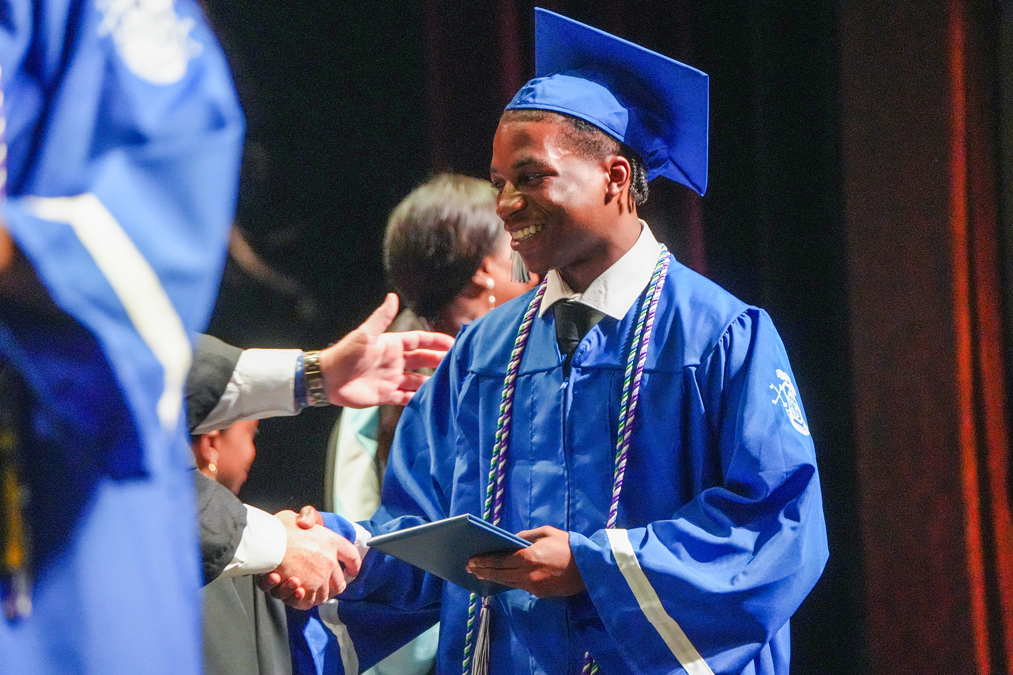 A person in a blue gown shakes hands with another person during a ceremony.