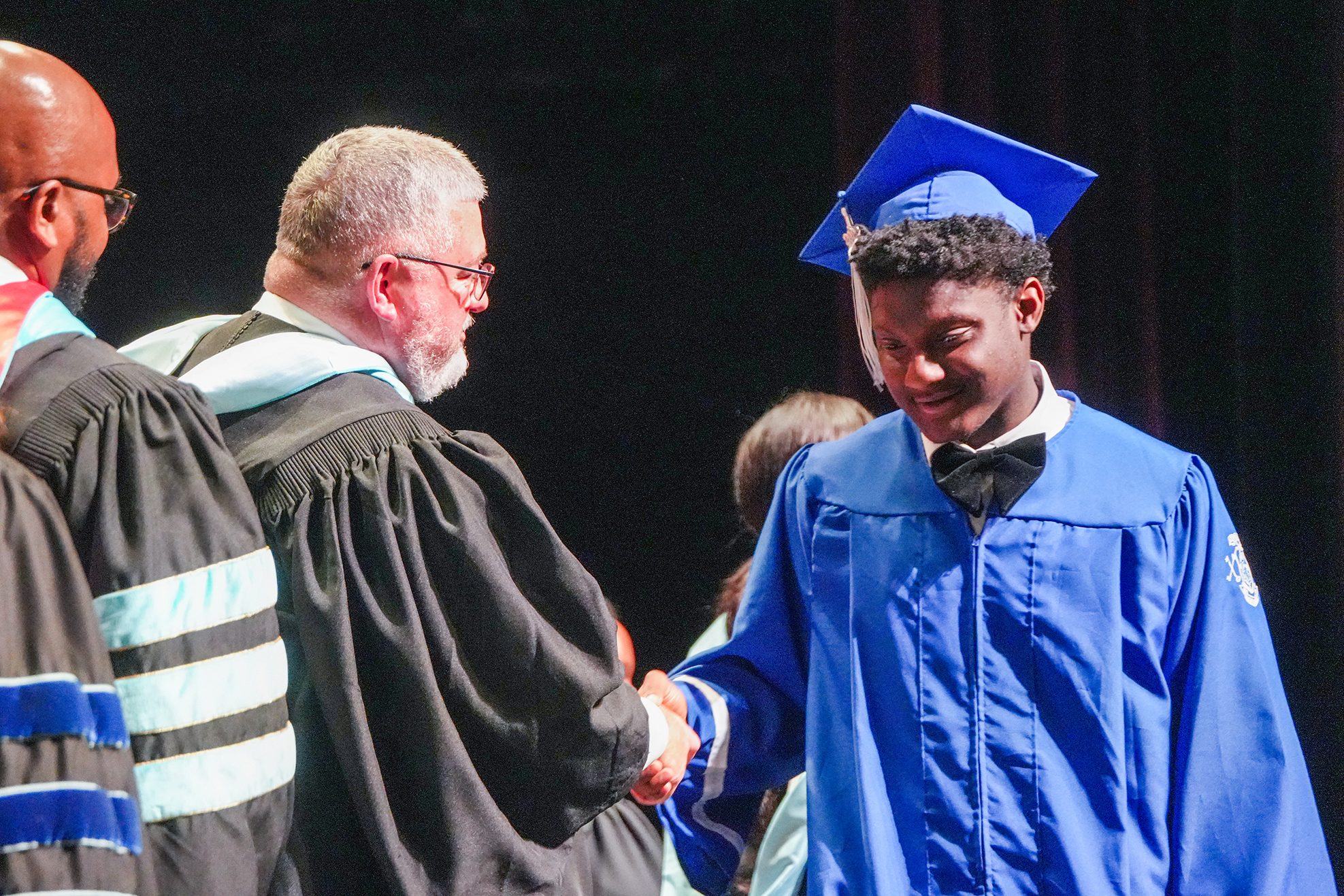 A man in a blue gown shakes hands with a man in a black gown at a ceremony.
