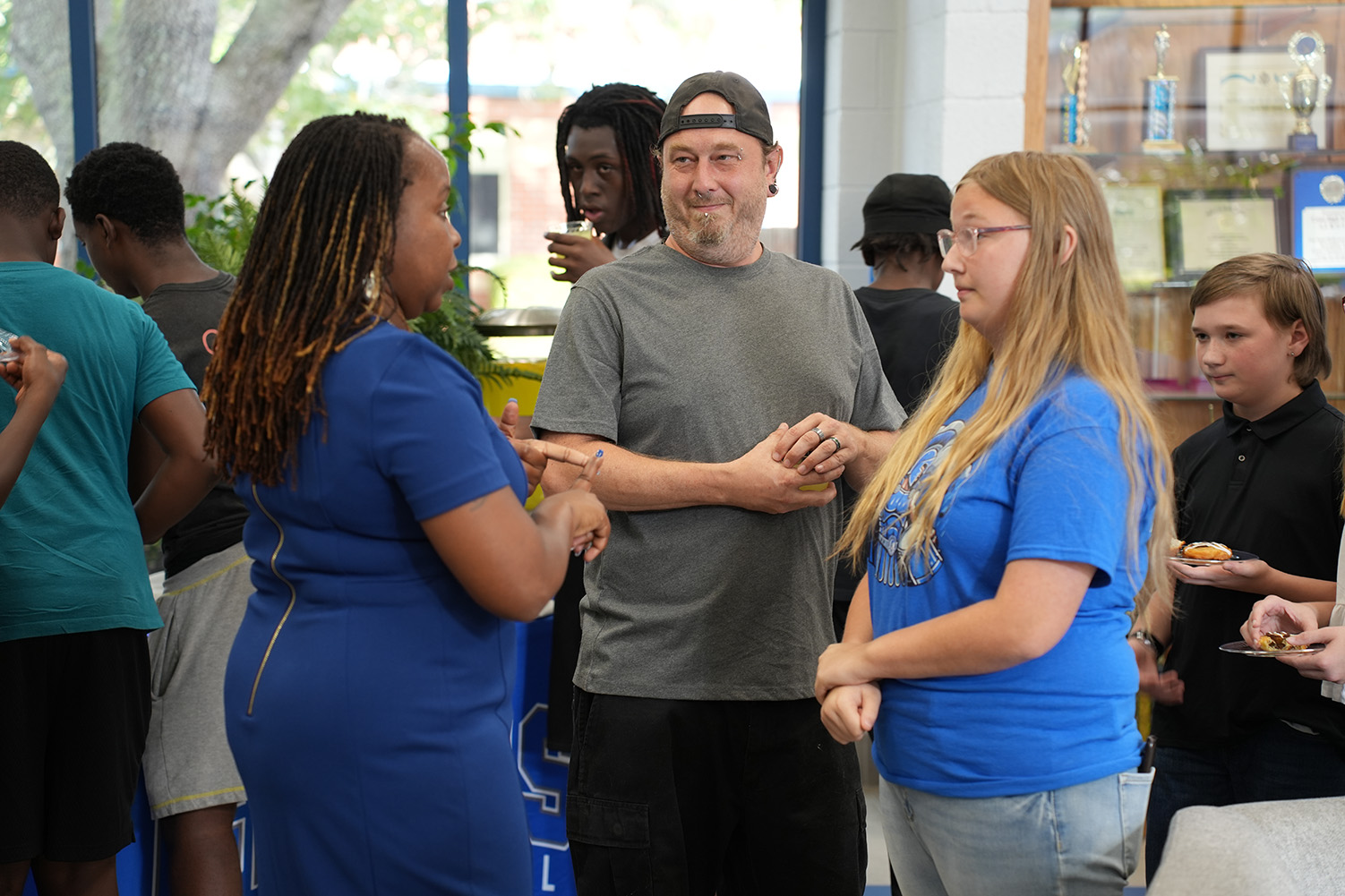 People at an event, with a man in a gray shirt and two women in blue shirts facing each other.