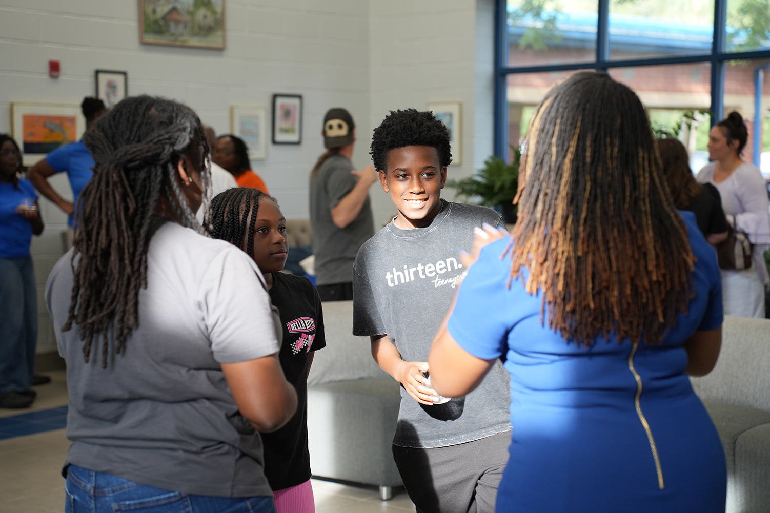 A group of people in a room with art on the walls. A boy wearing a gray shirt smiles.