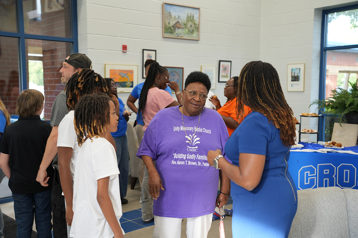 People conversing at an event, with a woman in purple and a woman in blue talking closely.