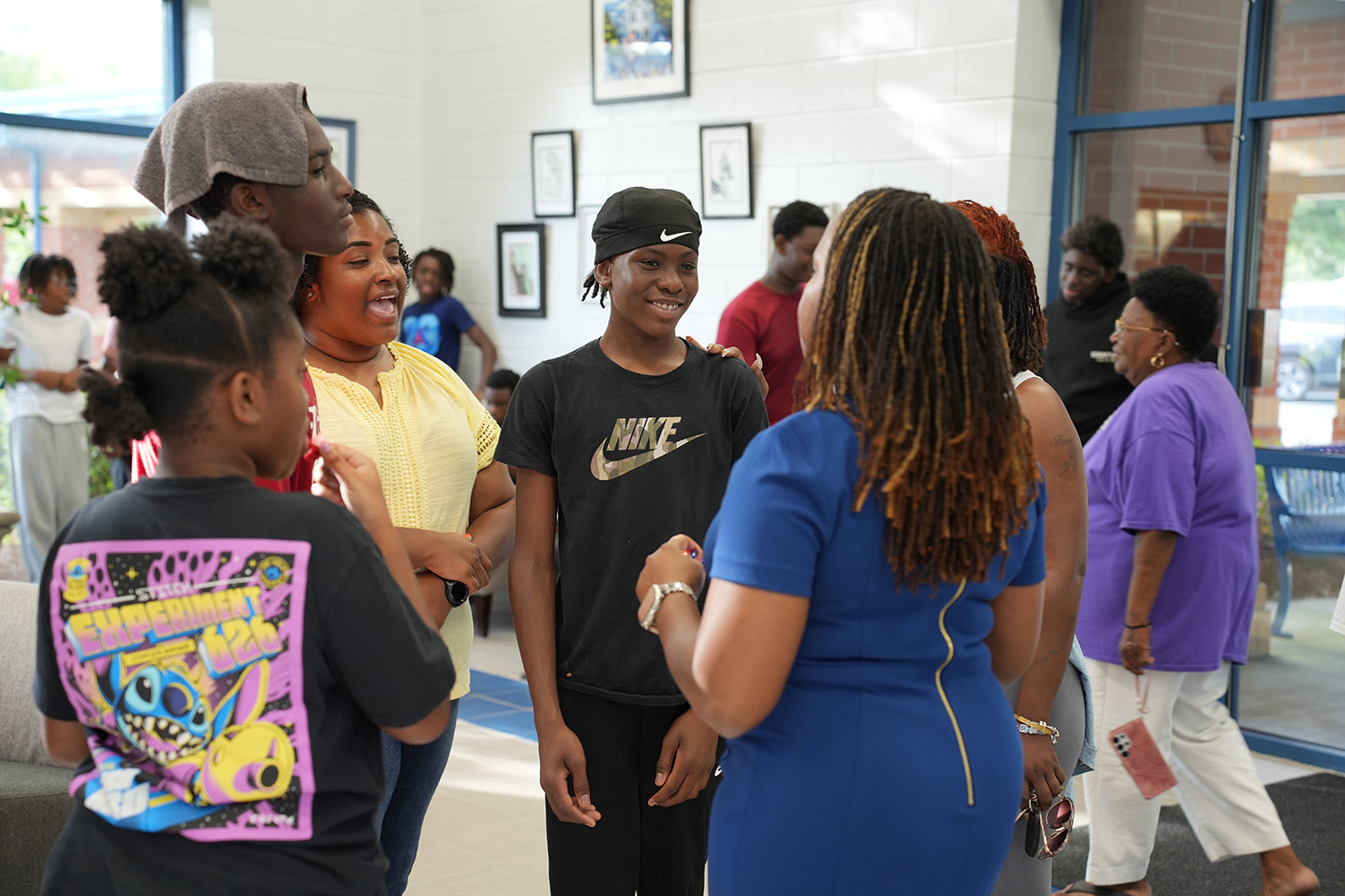 People conversing in a hallway; one woman wears a blue dress and the others wear casual clothing.