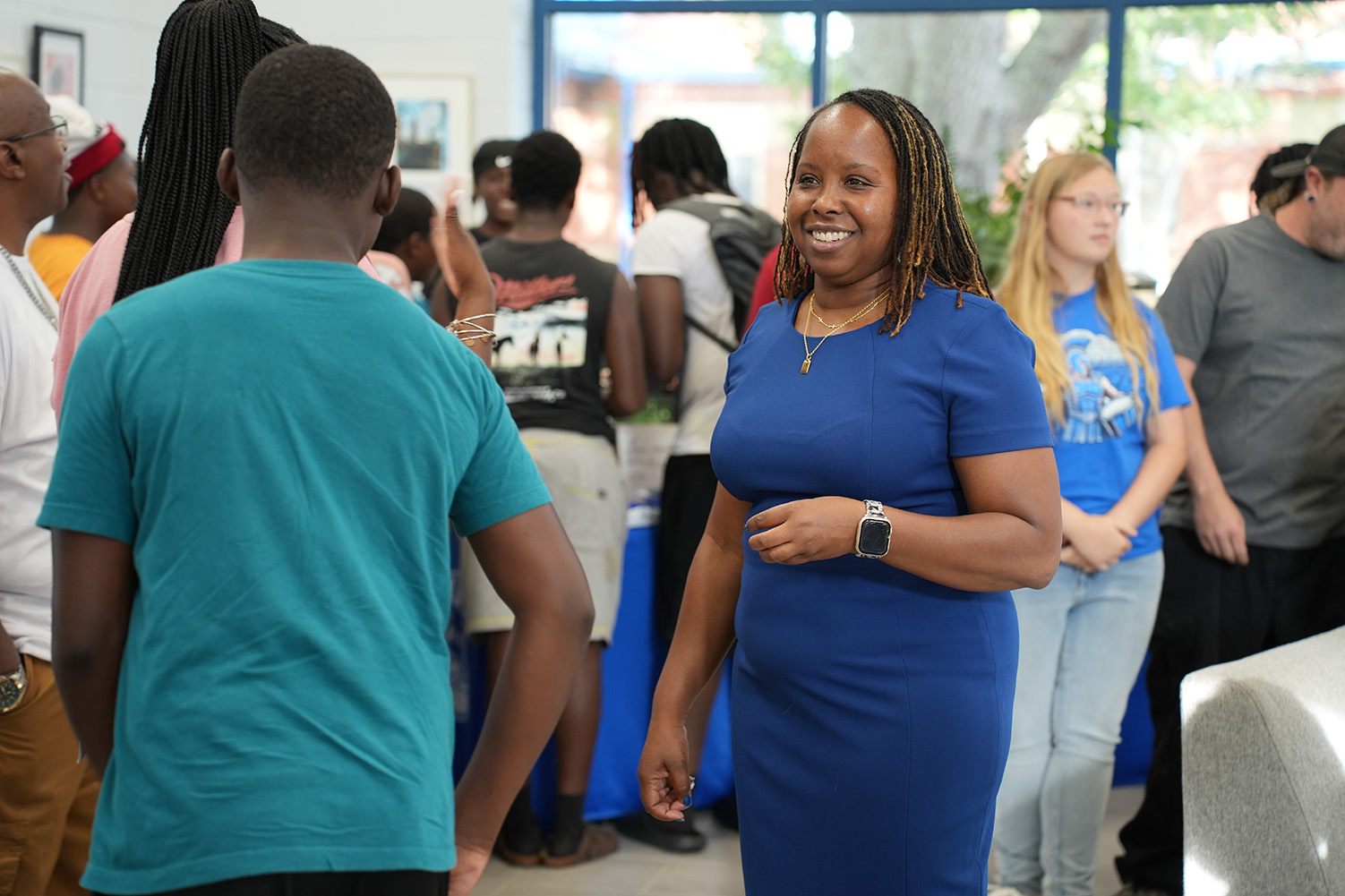 A woman in a blue dress speaks to a man in a teal shirt among a crowd.