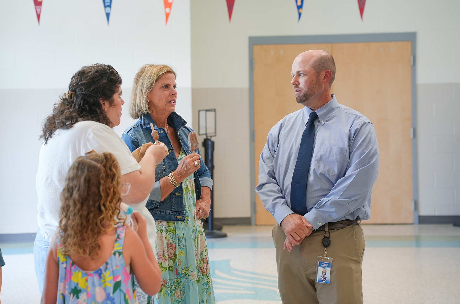 Four adults and a child stand in a hallway; two adults converse, and two listen. A flag hangs above them.