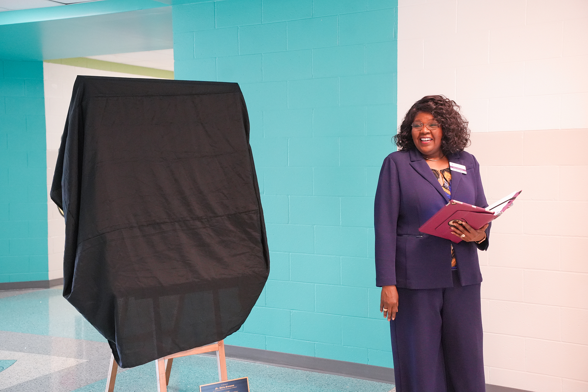 A woman in purple holds a book and stands next to a covered voting booth in a hallway.