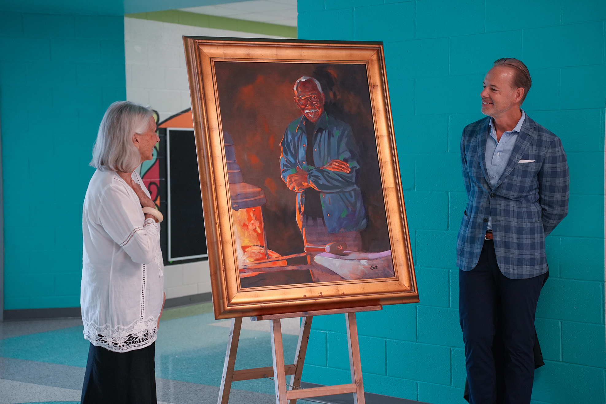 Two people view a large portrait of a man, who wears a blue jacket, on a stand.