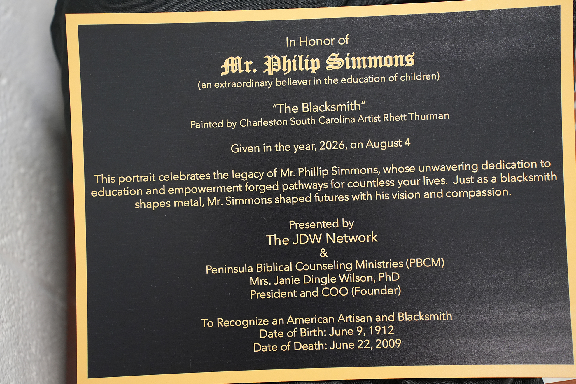 Black plaque with gold border. It reads, "In Honor of Mr. Philip Simmons, The Blacksmith." Birth and death dates are listed.