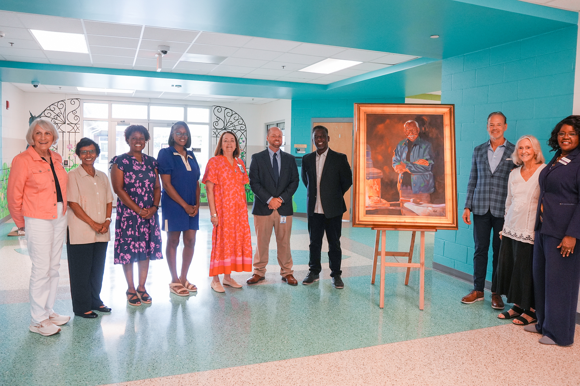 Nine people pose for a picture in front of a painting in a brightly colored room with a tiled floor.