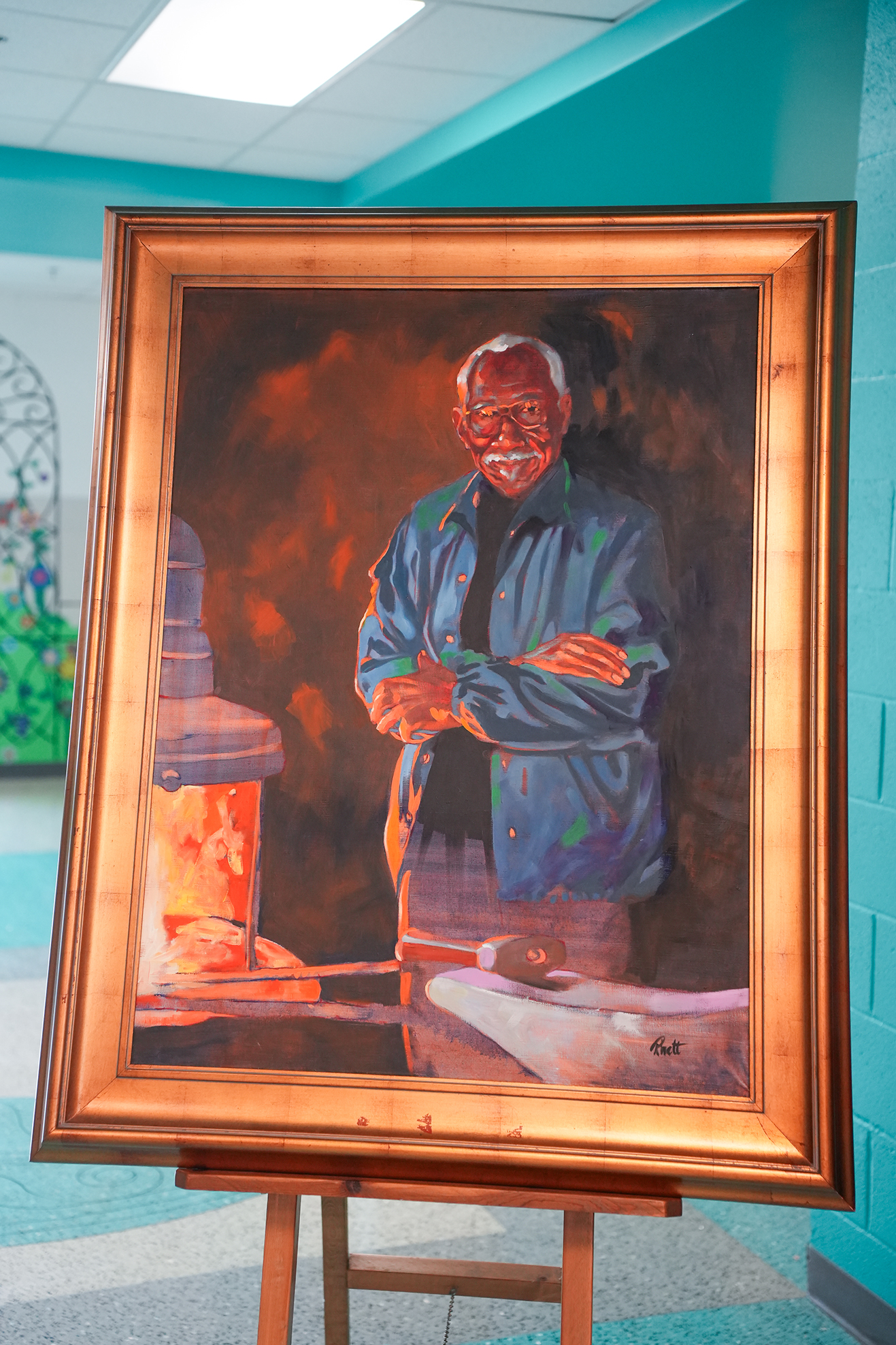 A large framed painting of an older man with a smiling face wearing a blue jacket with arms crossed. Background has blue walls.