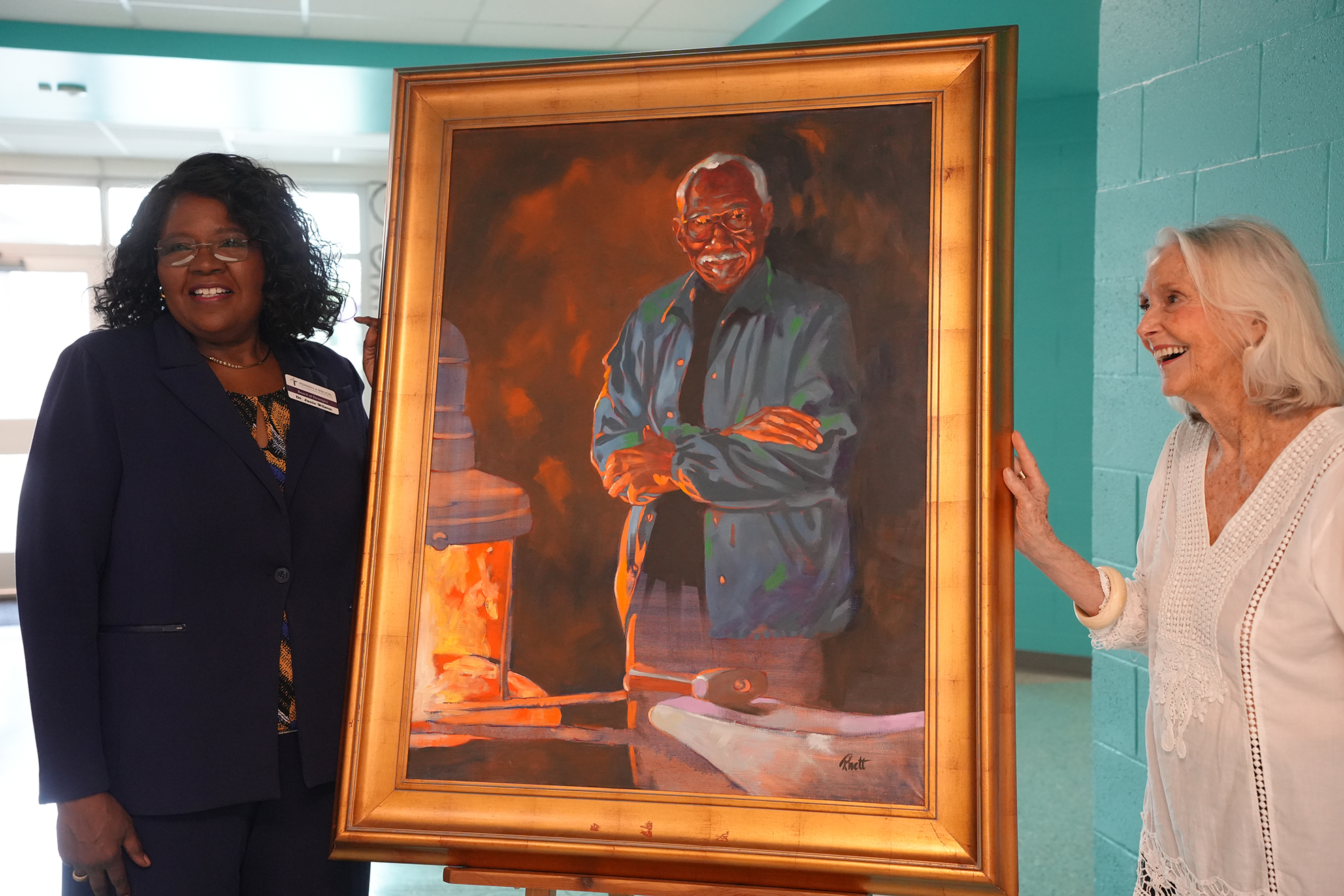 Two women stand by a large painting of a man in a blue shirt with arms folded.