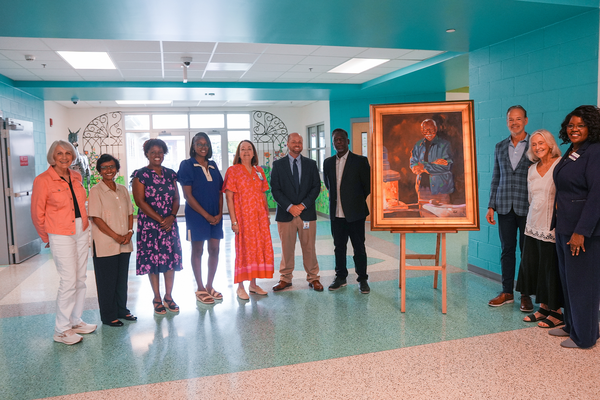 Nine people stand in a corridor. A portrait on an easel is in the center. Two arched windows are on the wall behind them.