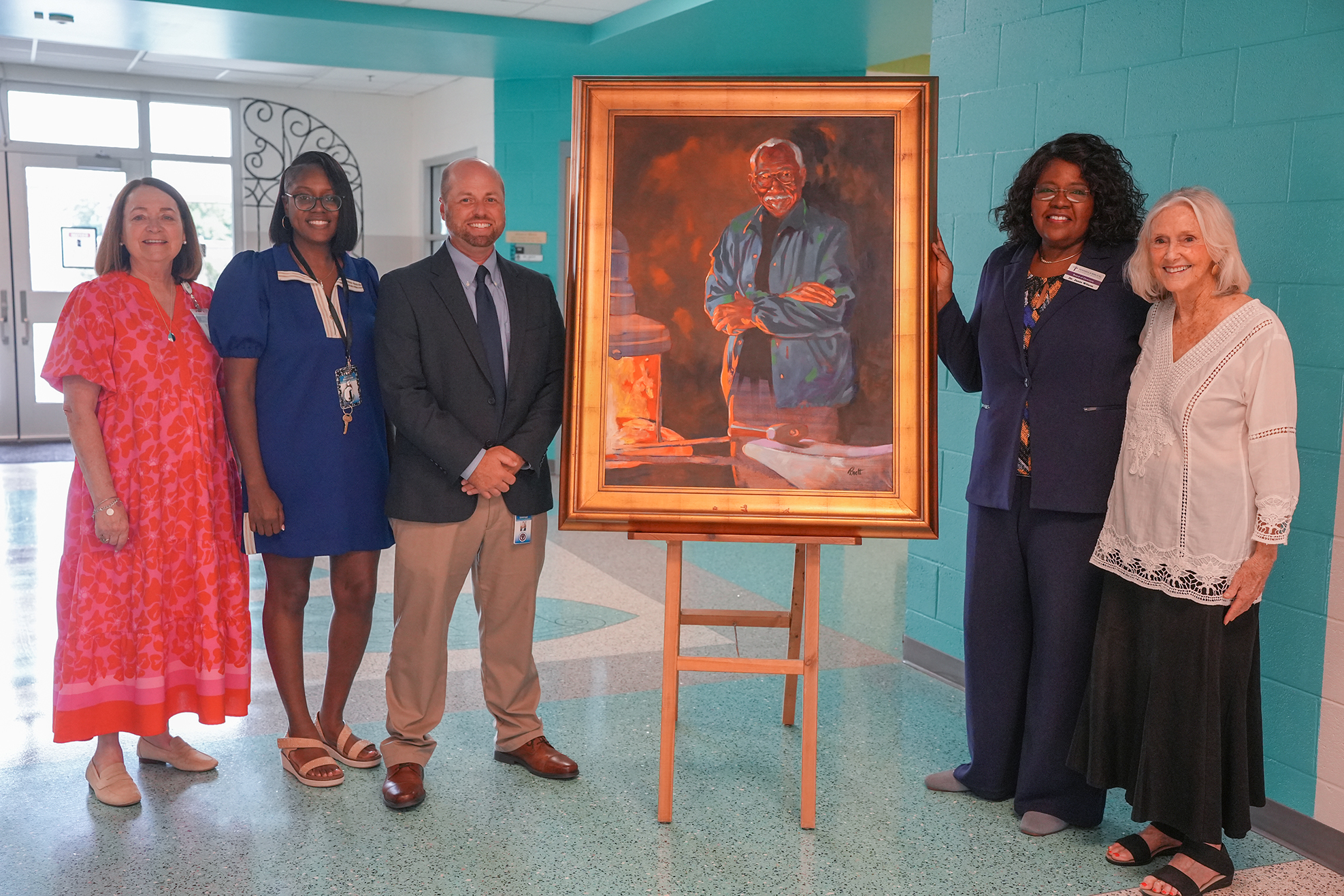 Five people stand behind a painting, three women in dresses and two men in suits. The painting depicts a man standing near a fire pit.