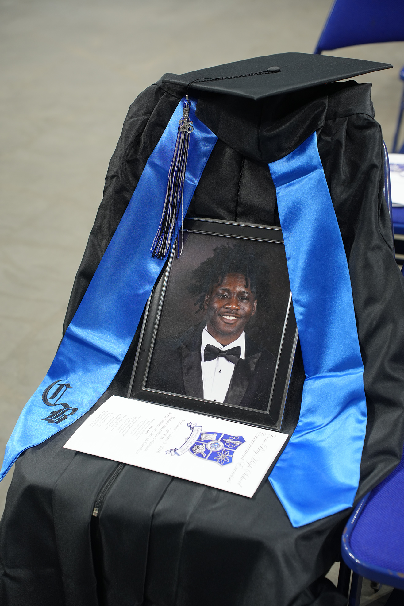 Black gown with blue sash and tassel, a framed photo of a person in a bow tie, and a white paper.