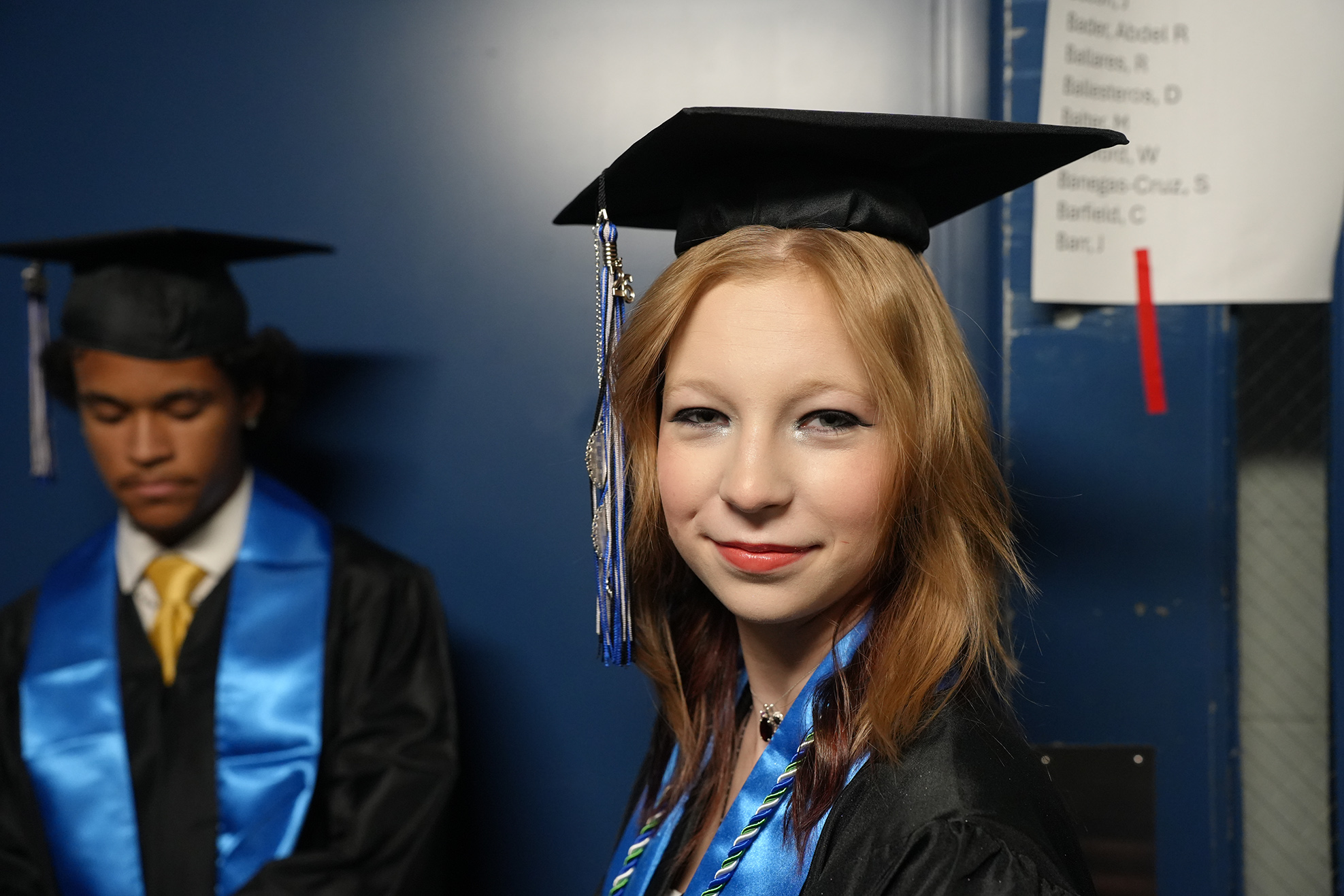 Two individuals in academic regalia; one with a blue tassel, the other with a yellow tie.