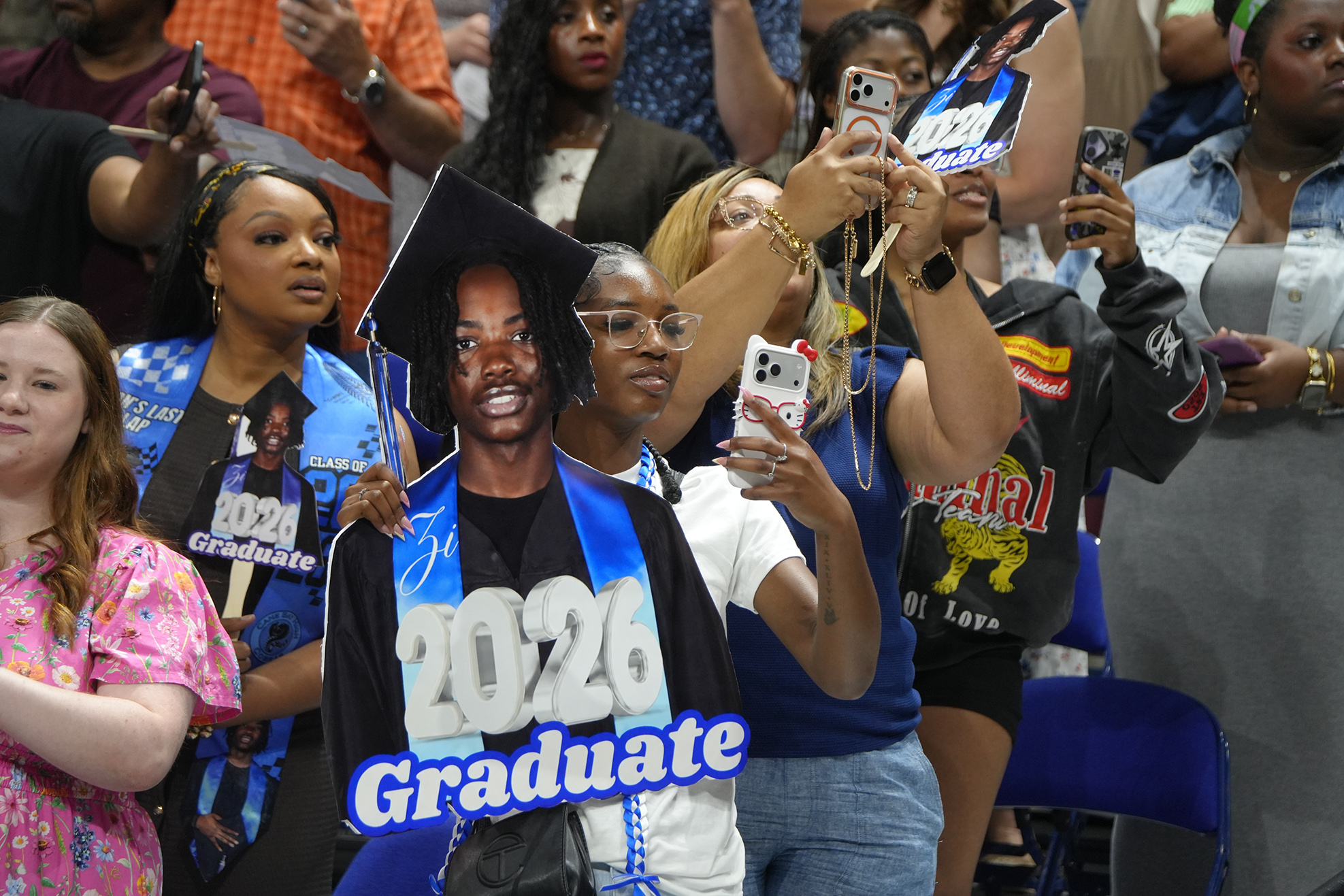 Group of people in an auditorium or stadium, with one individual dressed as a 2020 graduate.