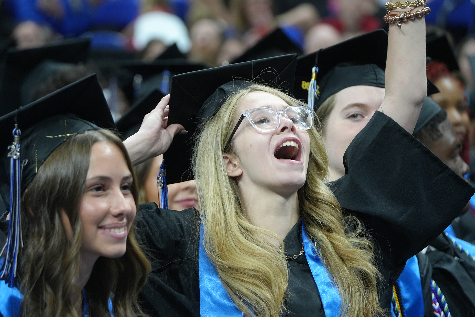 Graduates in academic regalia. One raises her arms in celebration. Another smiles at her.