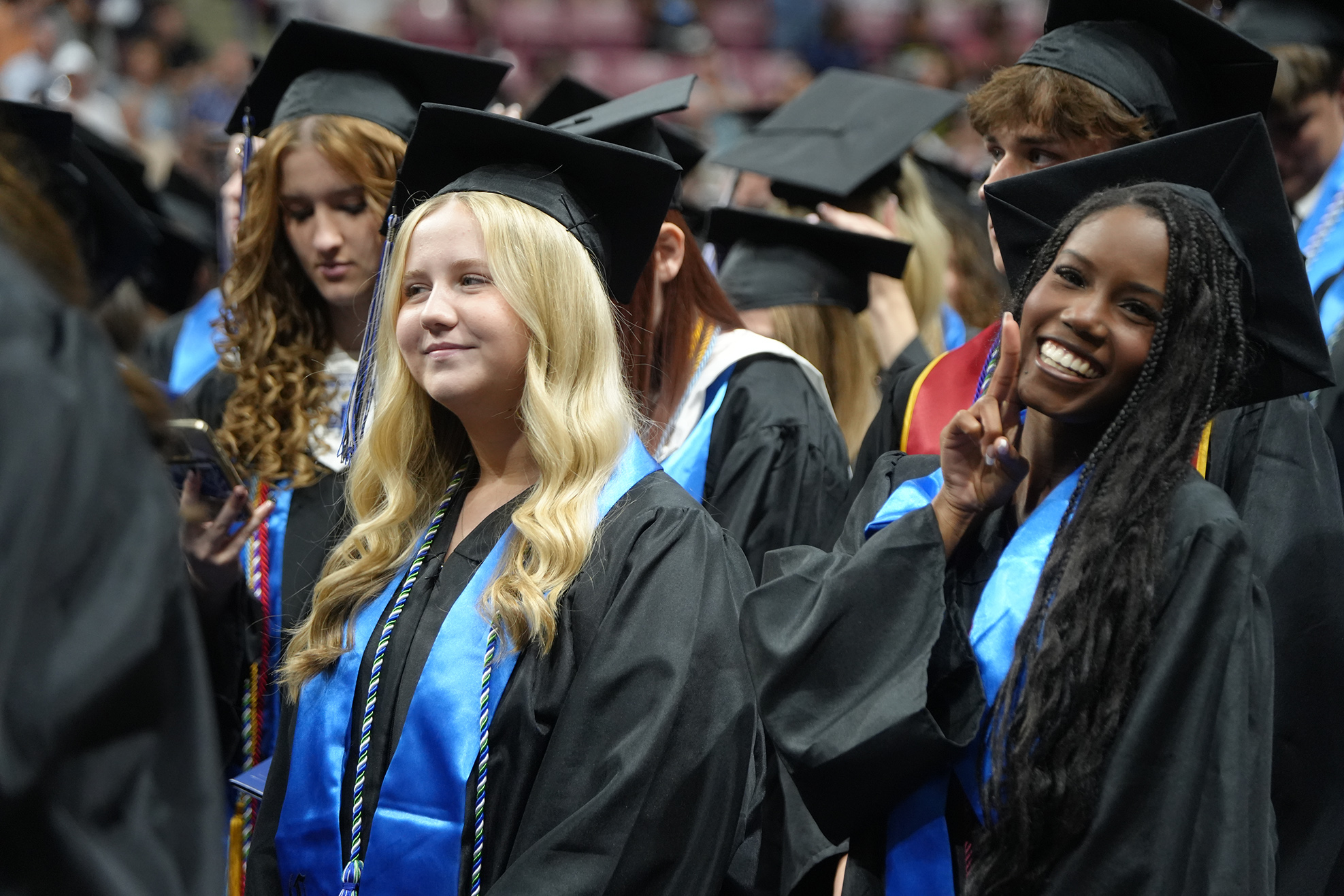 People in black gowns and mortarboards stand in a row, some smiling and looking ahead.