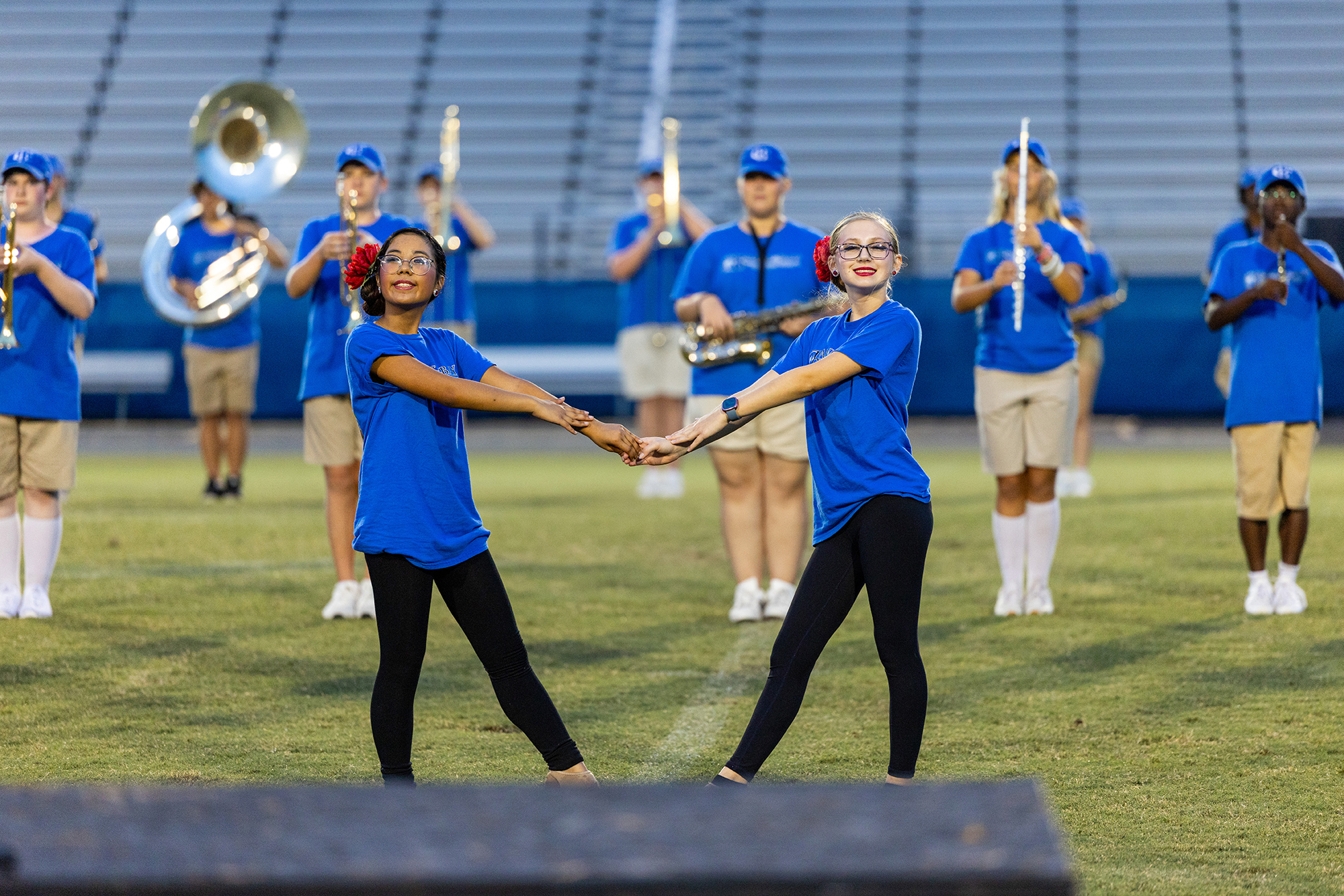A group of people in blue shirts and black pants holding hands while others play instruments on a field.