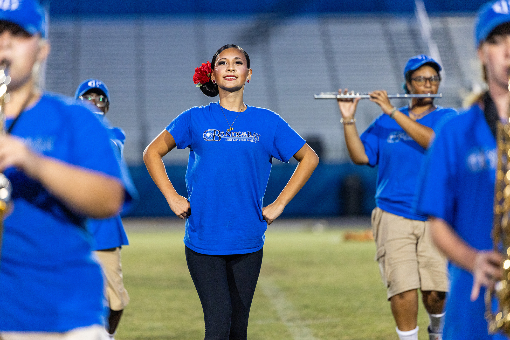 A group of musicians in blue shirts and black pants stand on a field, with some playing instruments.