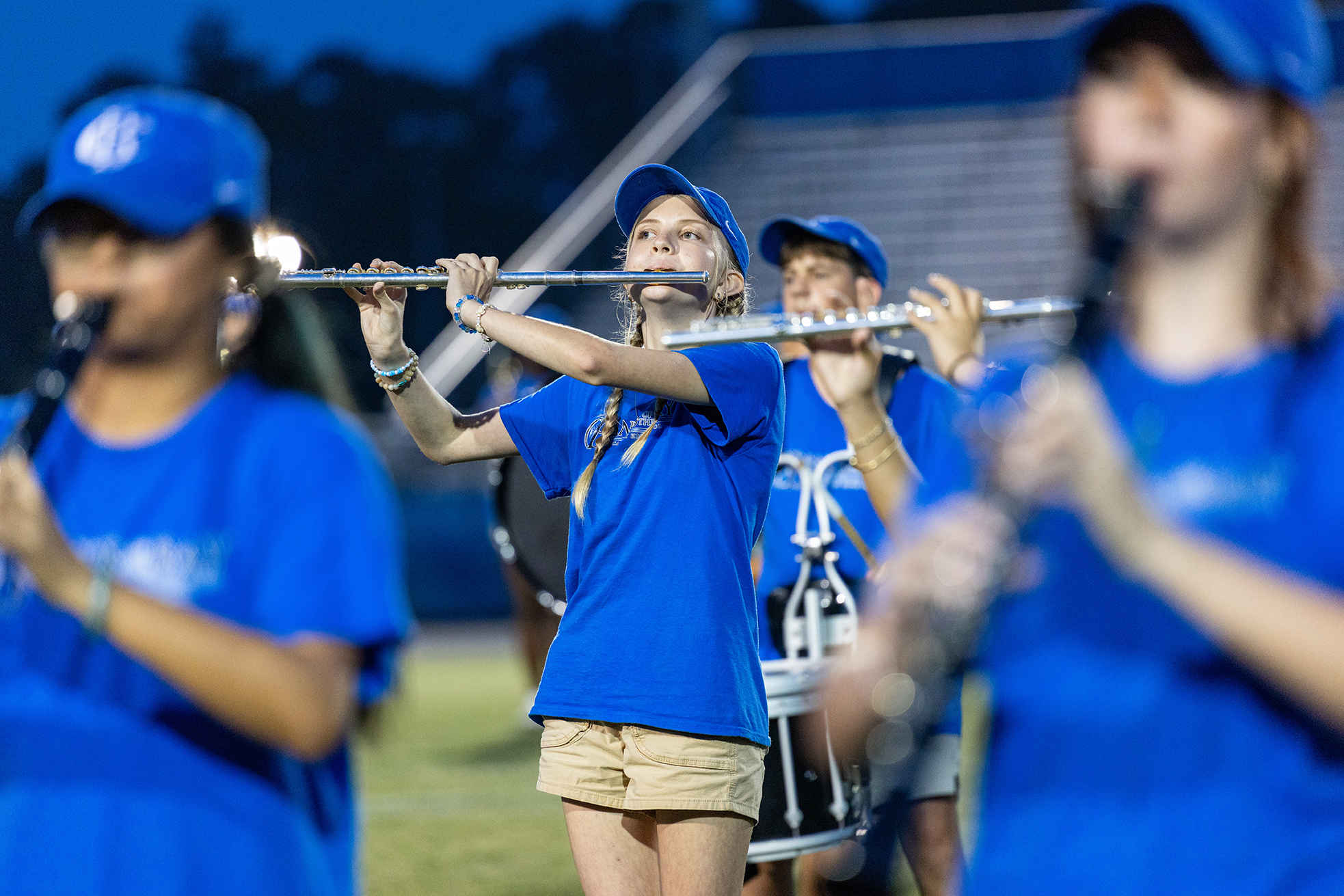 Four musicians in blue shirts and shorts play wind instruments on a field at night.