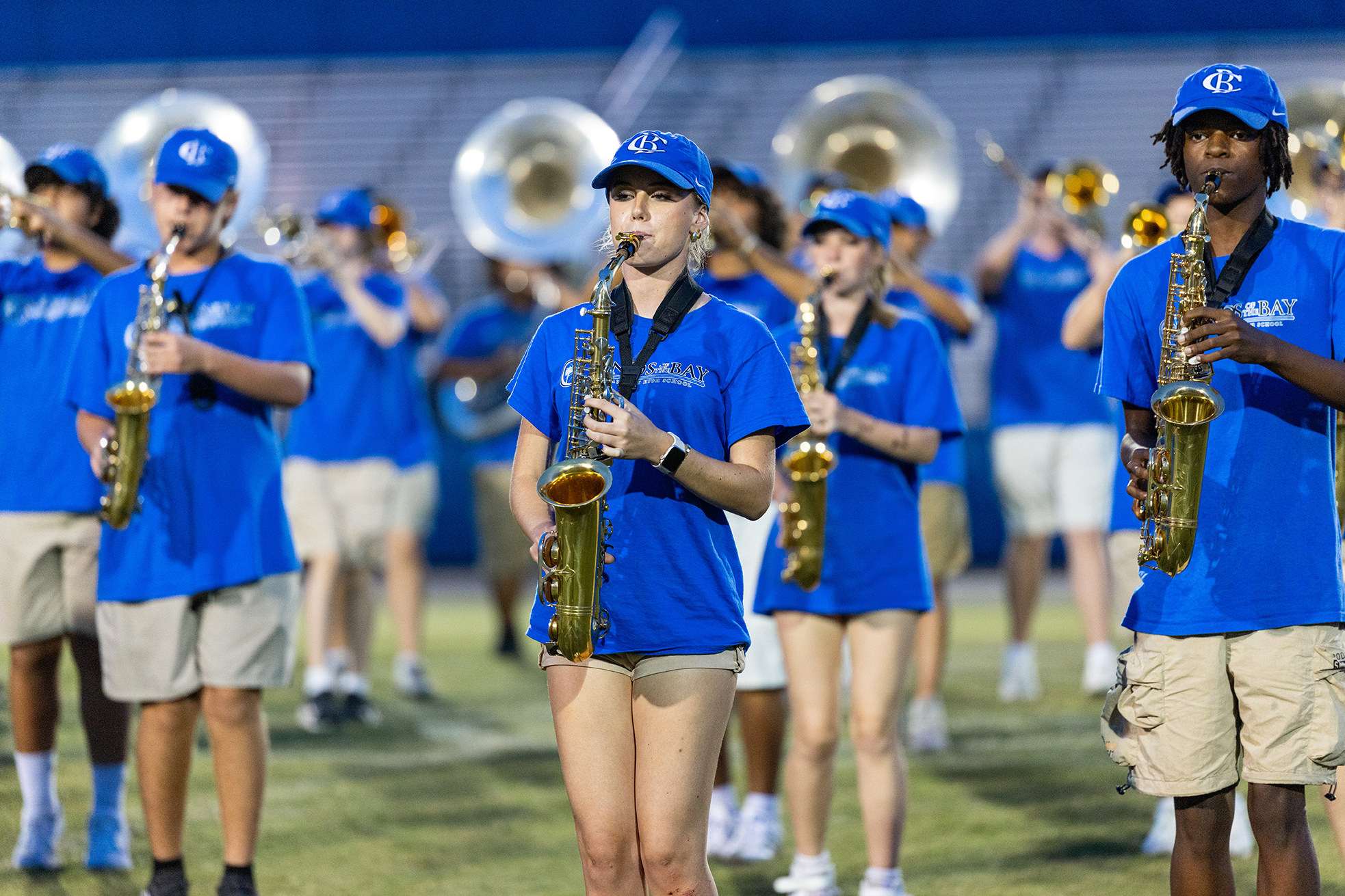 Several musicians in blue uniforms and caps play brass and woodwind instruments on a field.