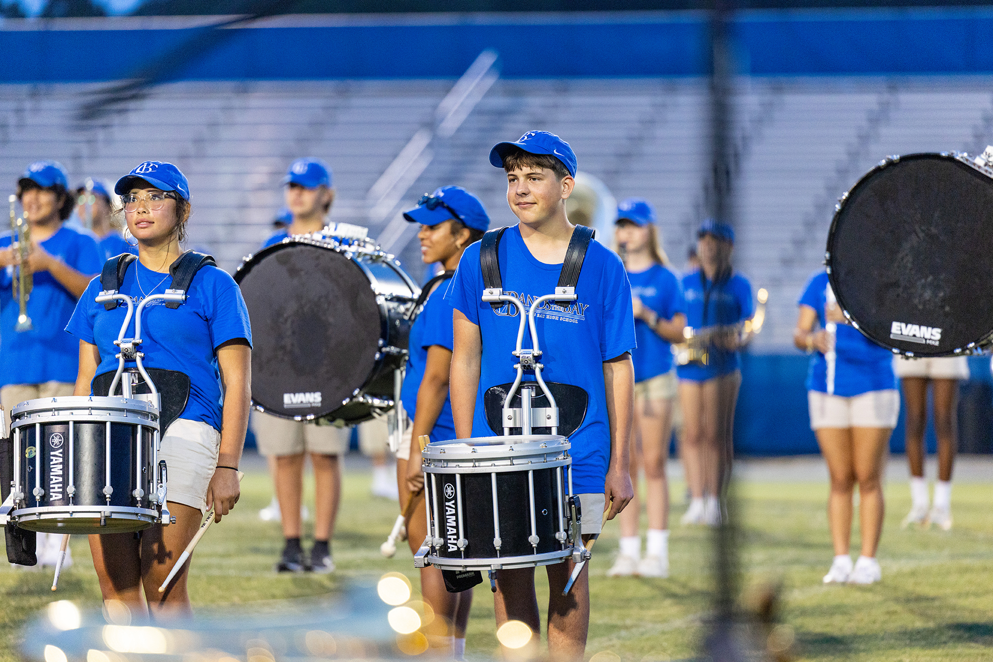 A group of people in blue uniforms, hats, and carrying drums on a field.