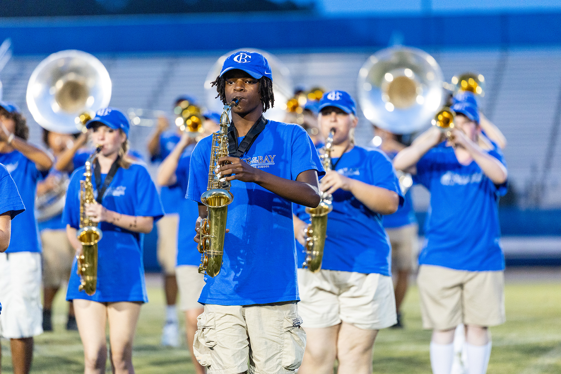 Band members wearing blue uniforms march on a field. Some play saxophones and others brass instruments.