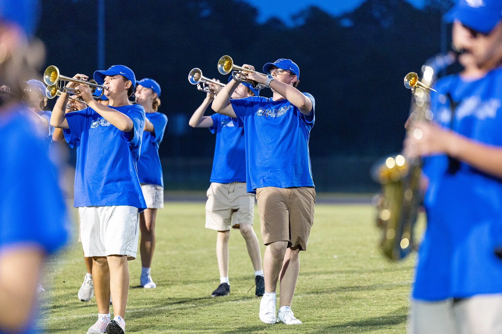 A group of people in blue shirts and caps play brass and wind instruments on a grassy field.