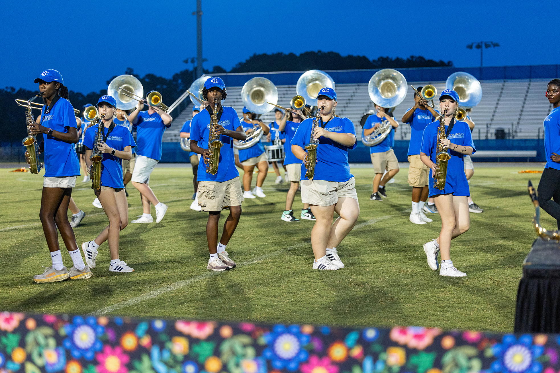 A marching band performs on a field with blue uniforms, holding instruments like trumpets and saxophones.