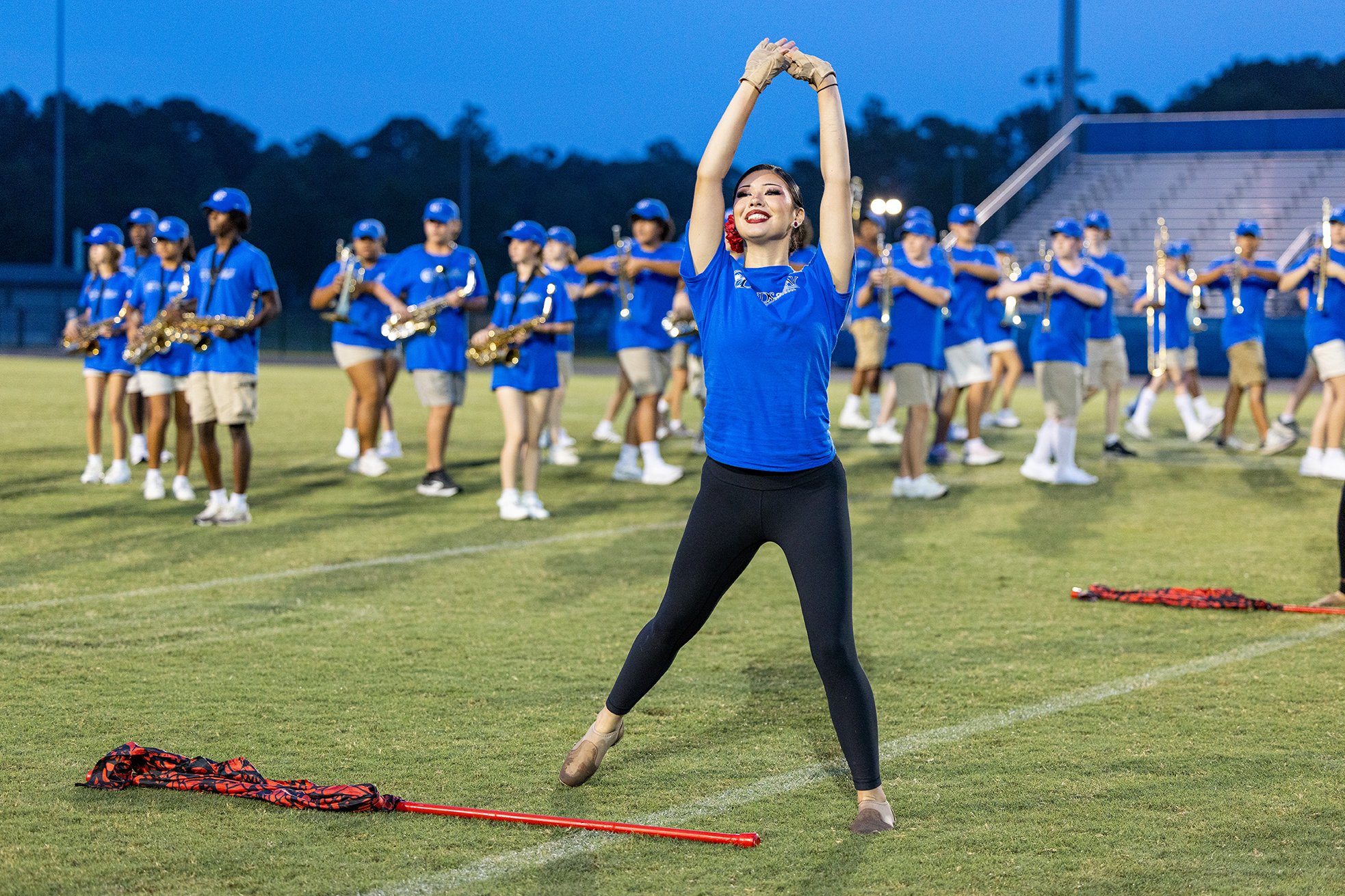 A woman stretches on a field as a band stands behind her on a football field.