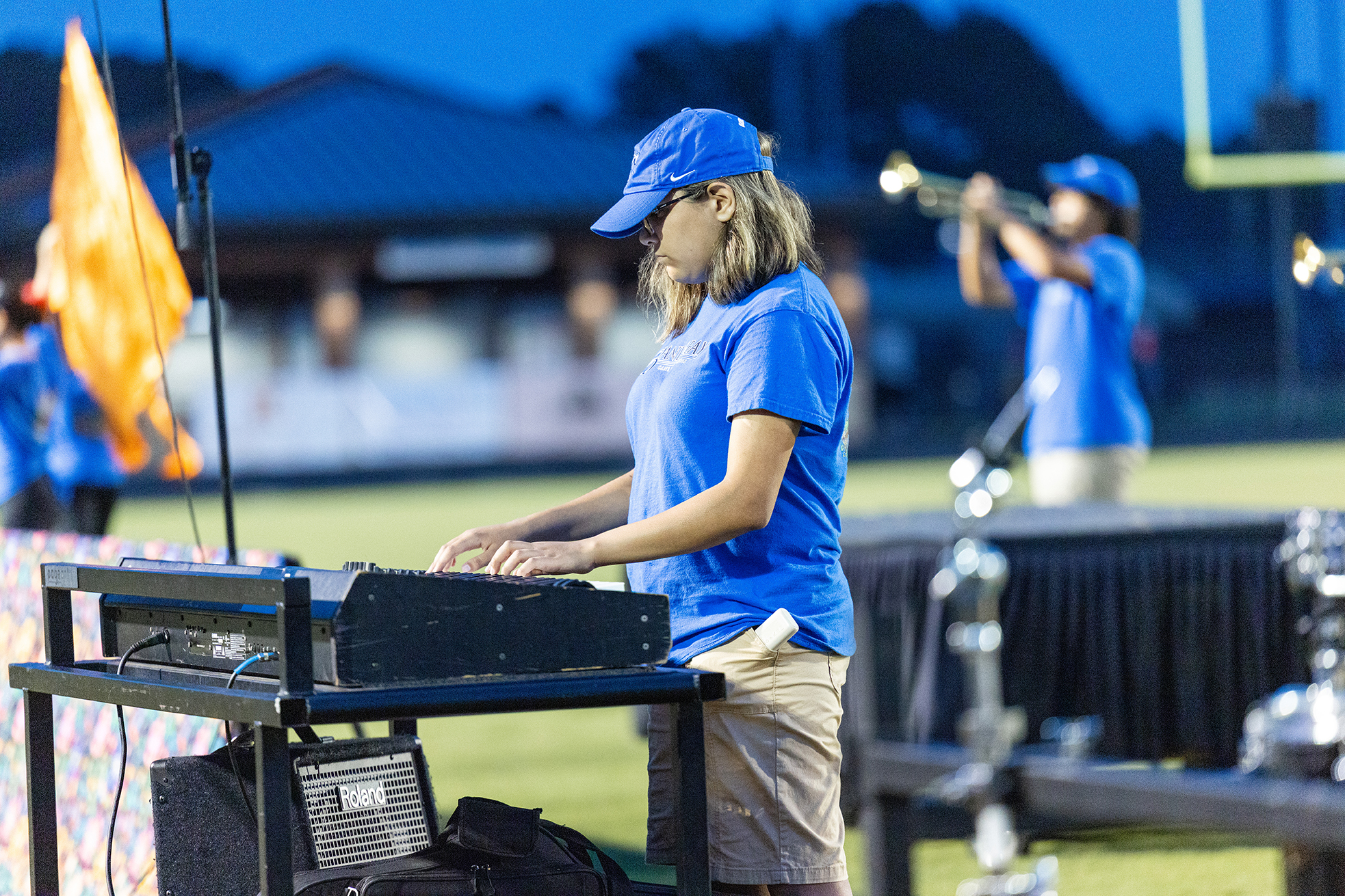 A woman plays a keyboard on a stand, with a trumpet player in the background.
