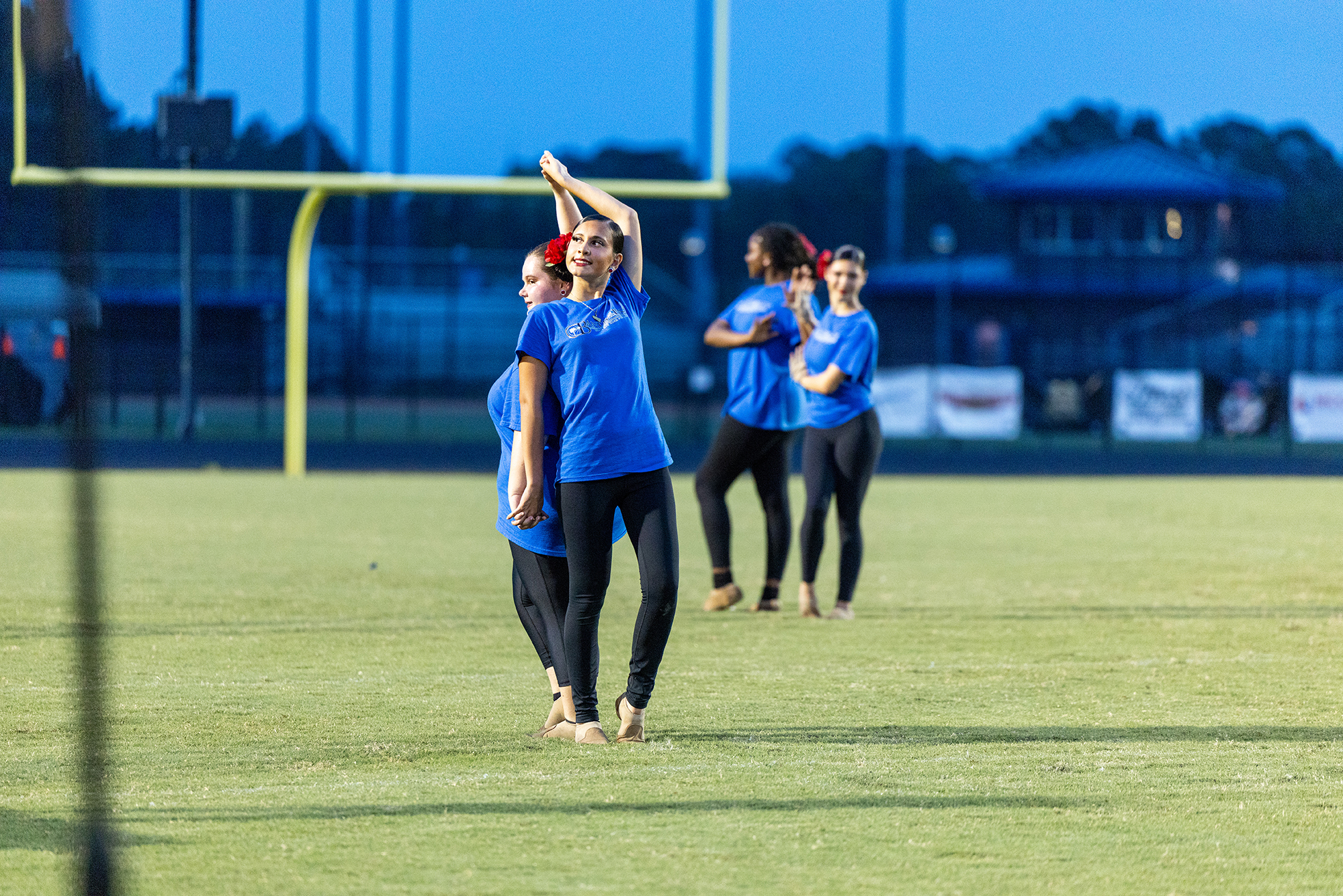 Four individuals in blue shirts and black pants perform a dance routine on a football field.