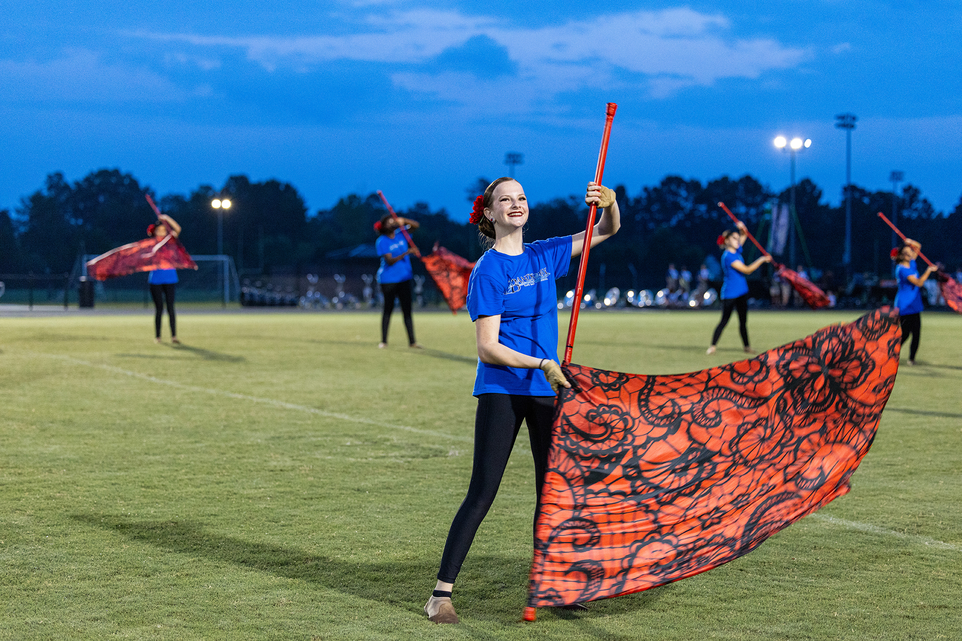 Woman in blue shirt and black leggings holding a red and black flag on a football field.
