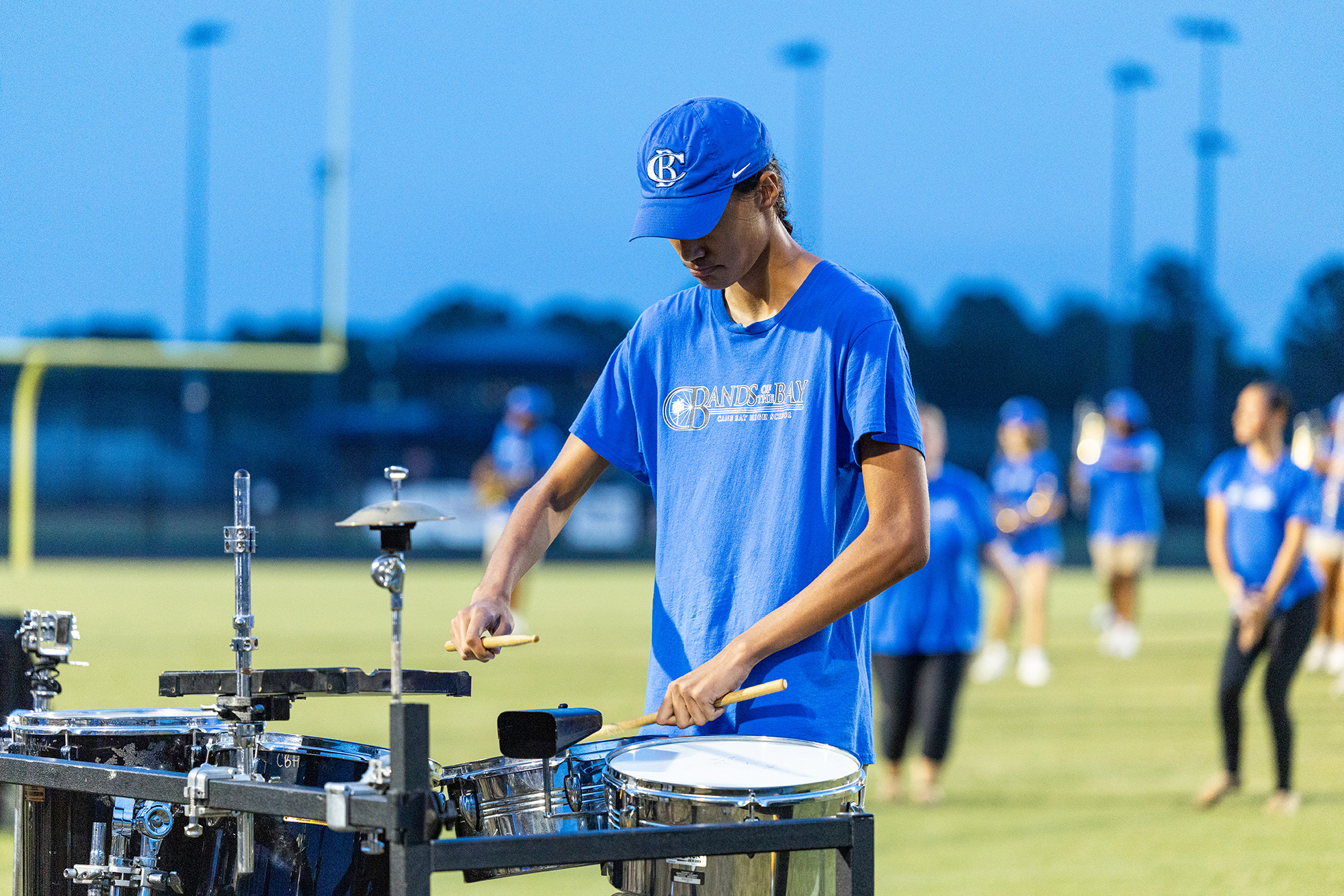 A man in a blue shirt and hat plays a drum set on a football field.