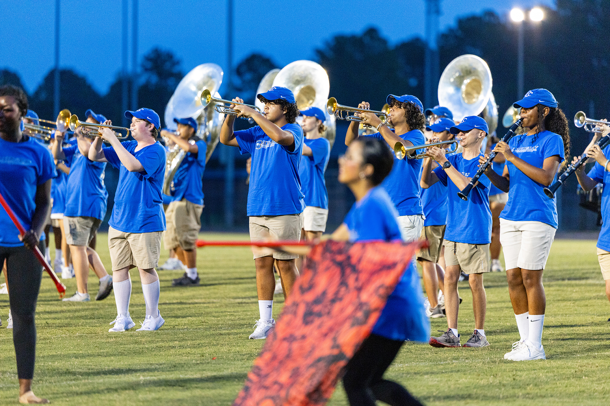 A group of people in blue shirts and white pants play instruments on a field at night.