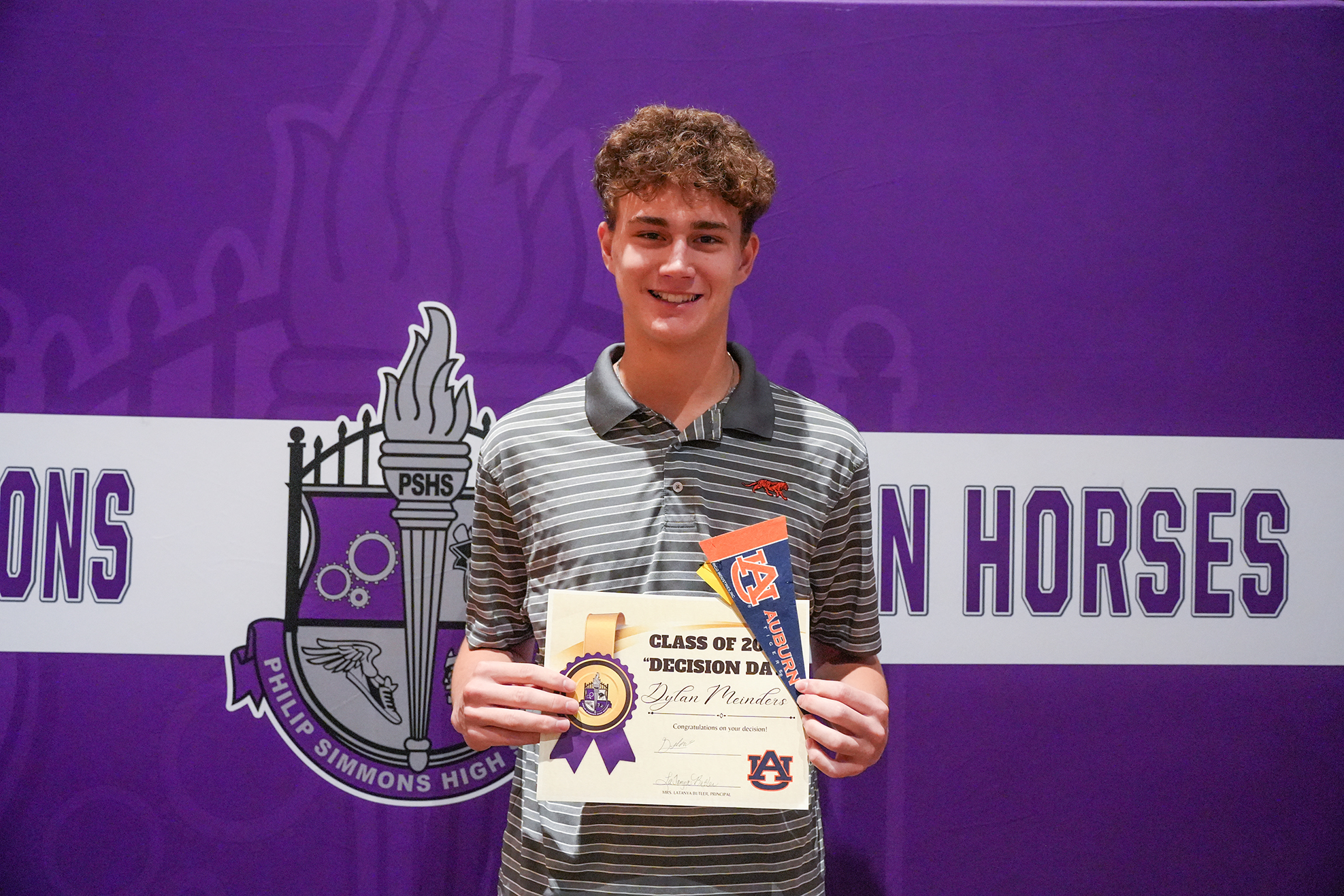 A person holds a certificate with "Class of 2023" on it. They wear a striped polo shirt.