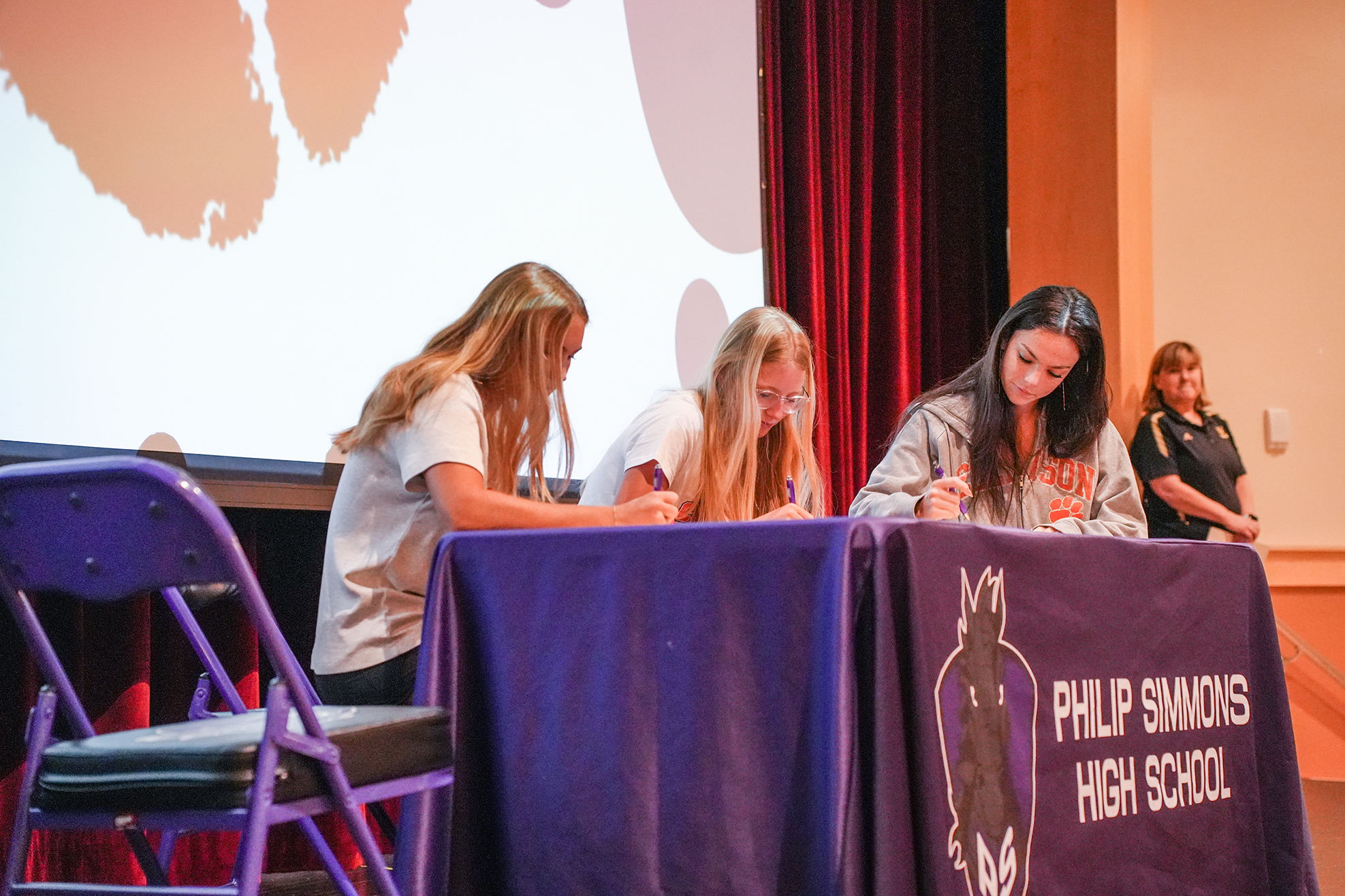 Four women seated at a table with a sign reading "Philip Simmons High School" write on paper.