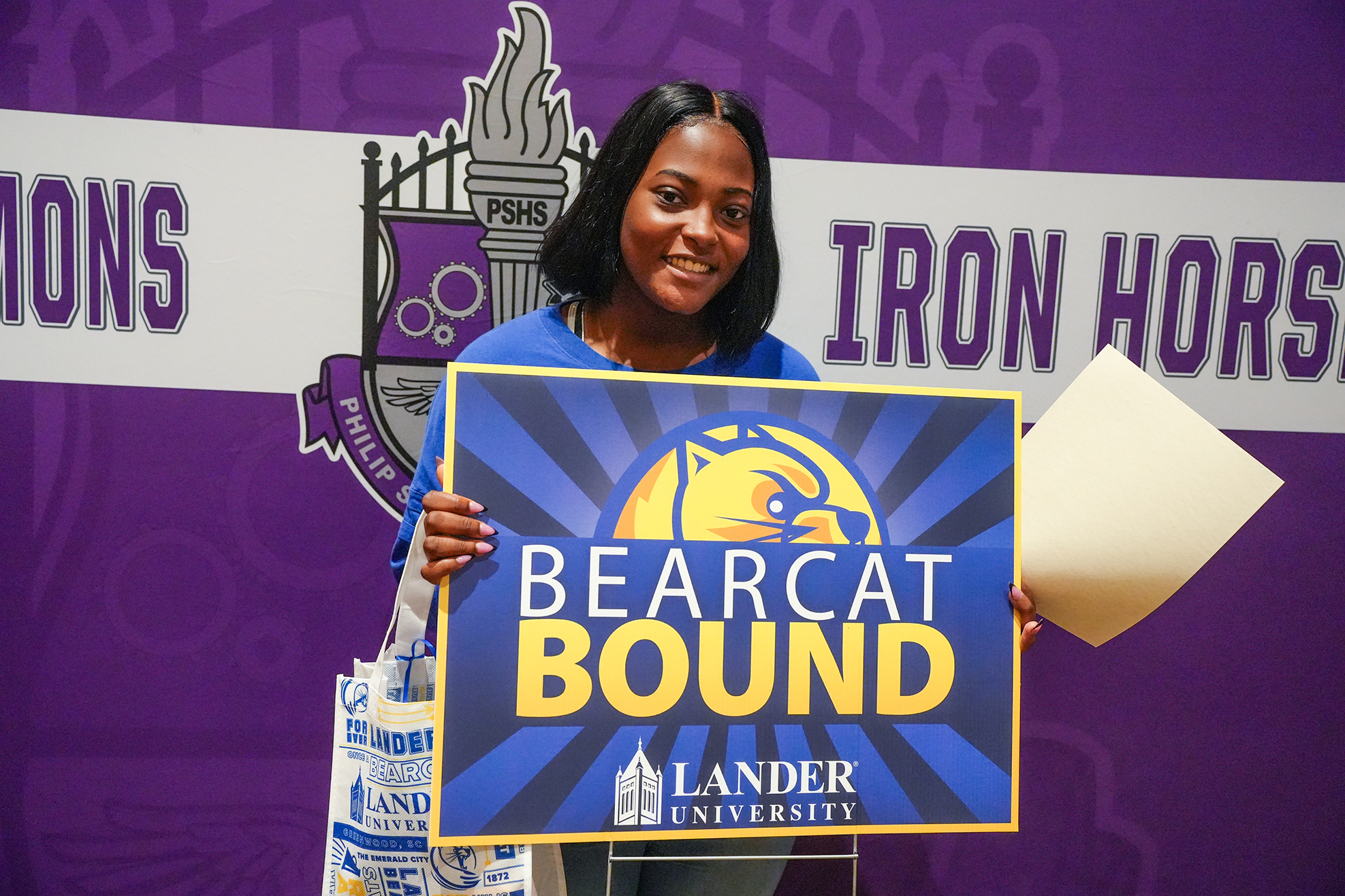 Woman holds a blue sign with the words "Bearcat Bound" in front of a purple backdrop.
