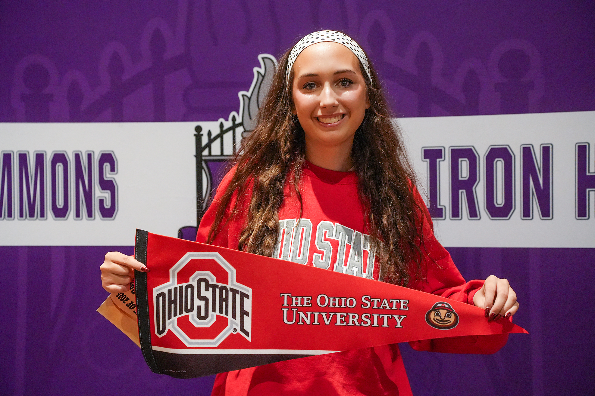 Woman with long hair holds a red banner with white text. The banner says "Ohio State". The background is purple.