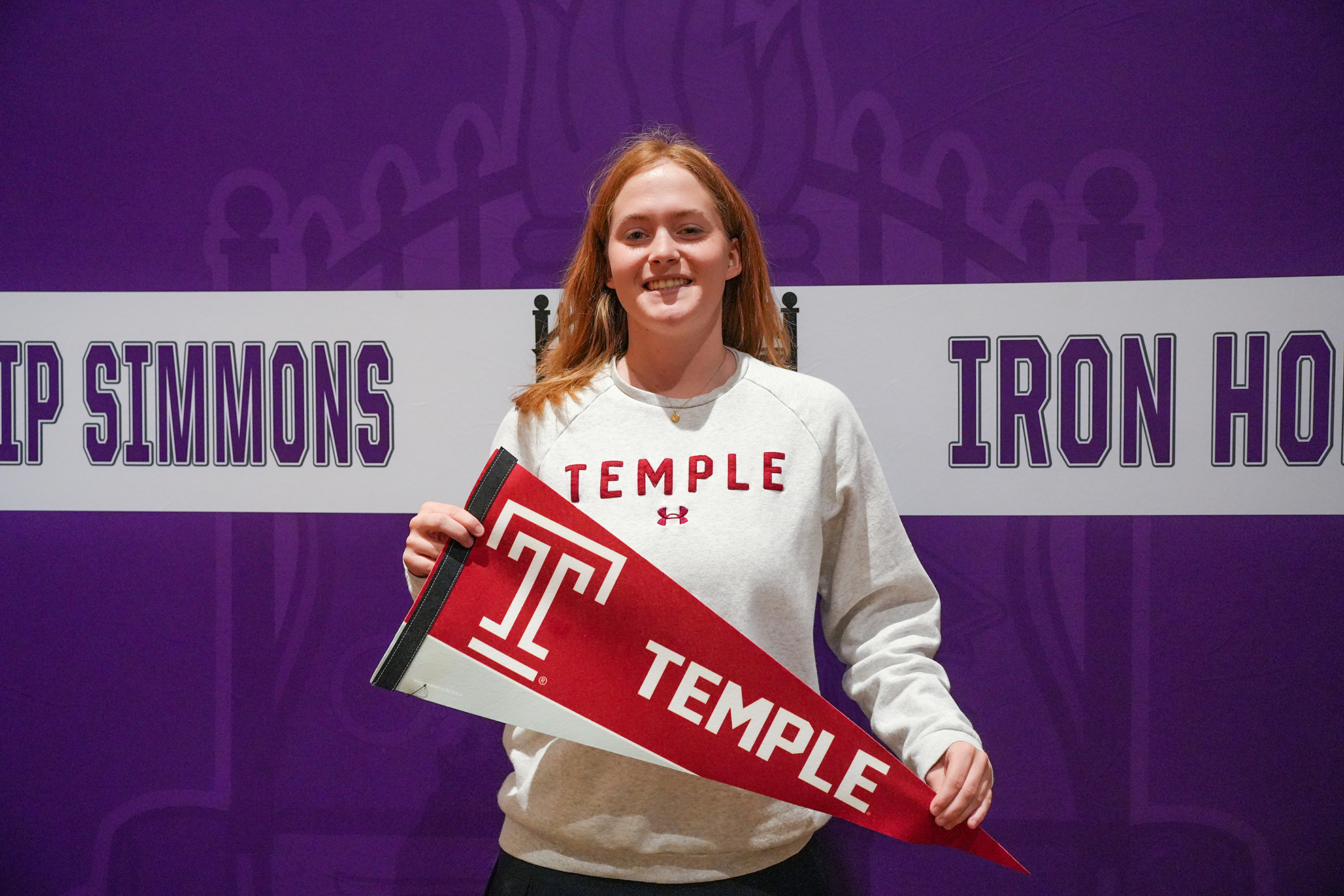 Woman holding a Temple University pennant in front of a purple backdrop with "Temple Simmons" and "IRON HO" text.