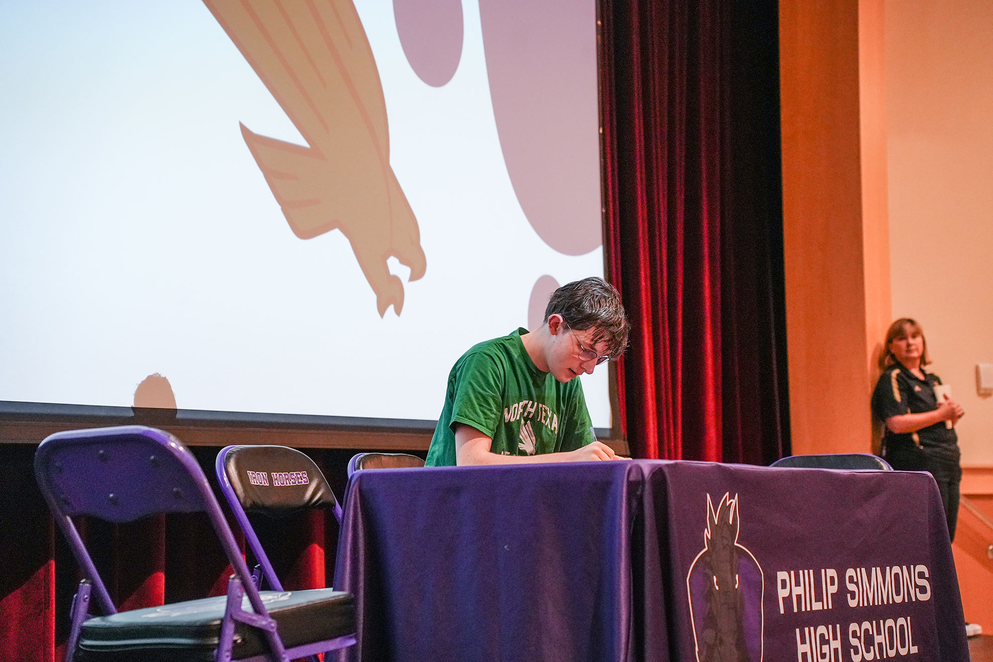A young person sits at a table under a projector screen displaying an image of a bird.