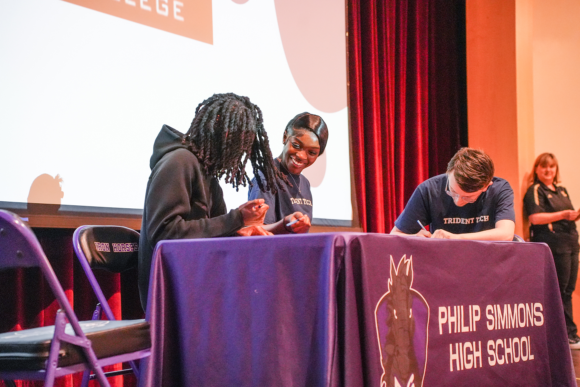 Students signing documents at a table with a purple tablecloth and Philip Simmons High School logo.
