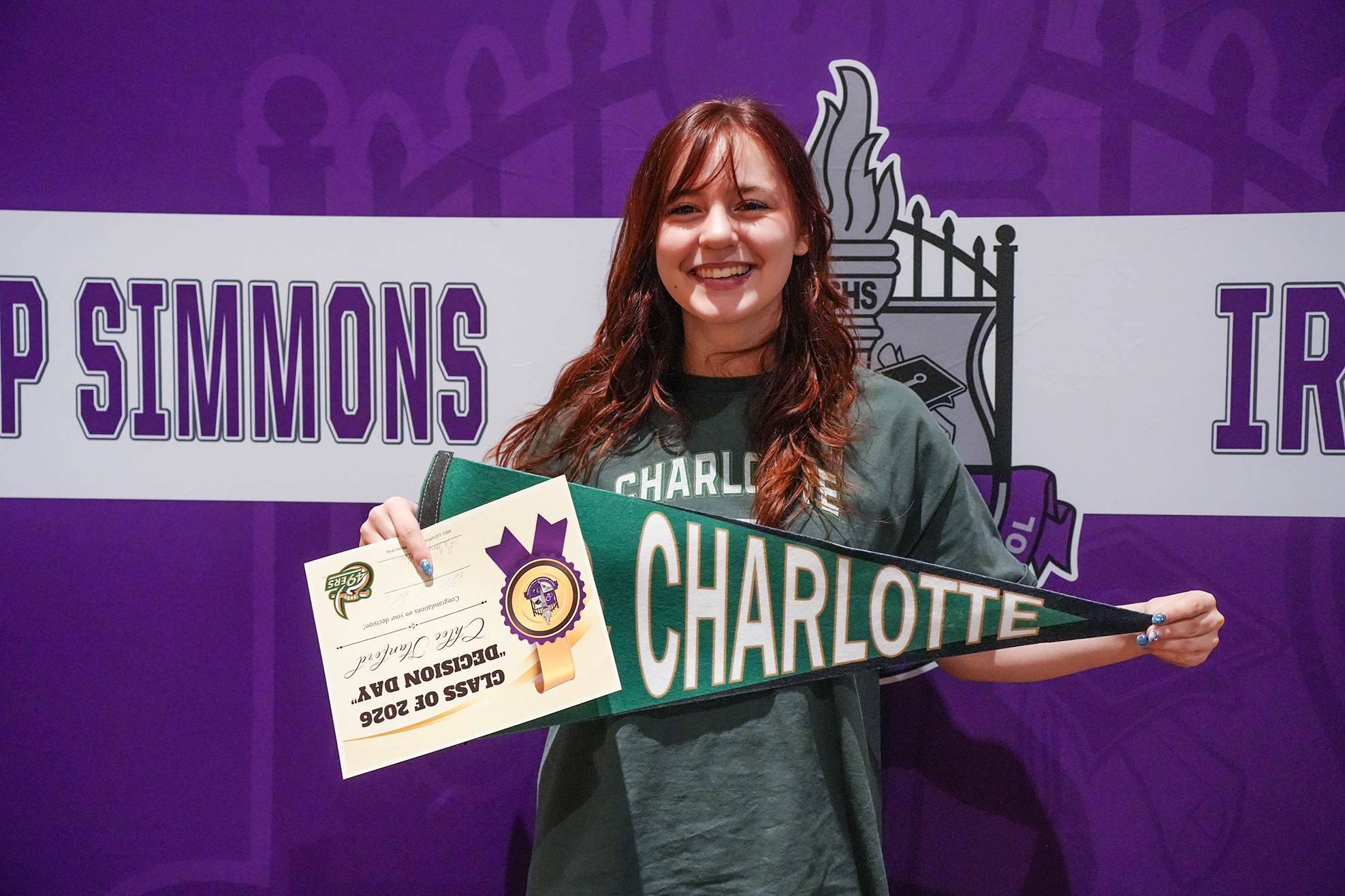Woman holds green banner with name "CHARLOTTE" and certificate with "Jane Doe Award" in front of banner reading "P SIMMONS".