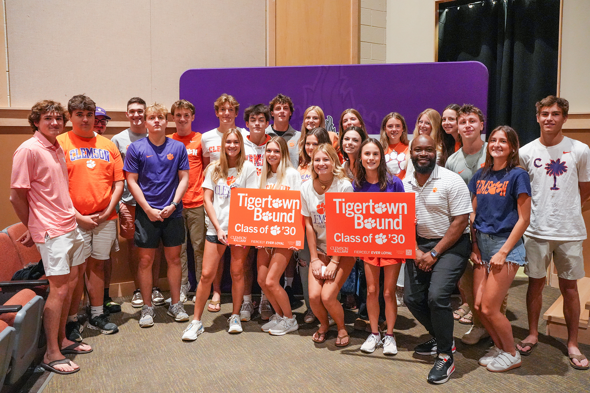 Group of students and a coach posing for a photo with purple backdrop and signs reading "Tigertown Bound Class of '20".