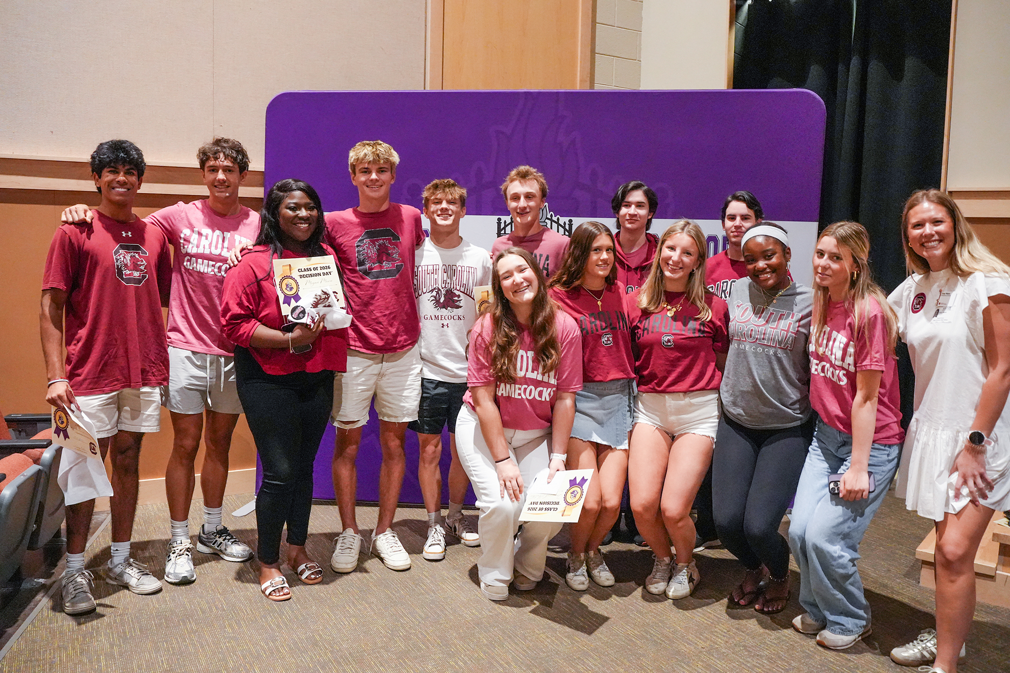 A group of individuals wearing red shirts and shorts, standing and posing for a photo in a room.