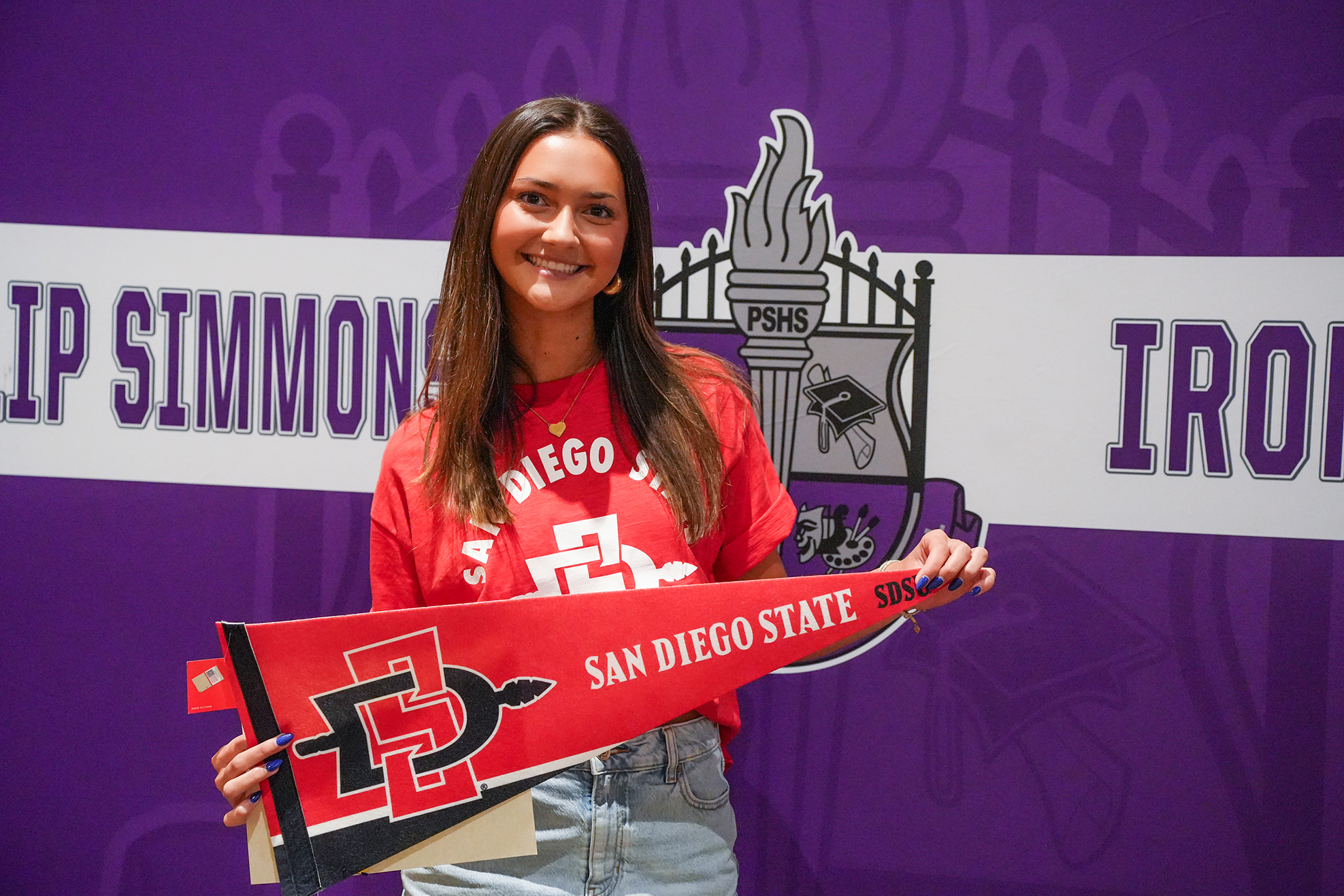 A smiling woman holds a San Diego State banner in front of a purple and white backdrop.