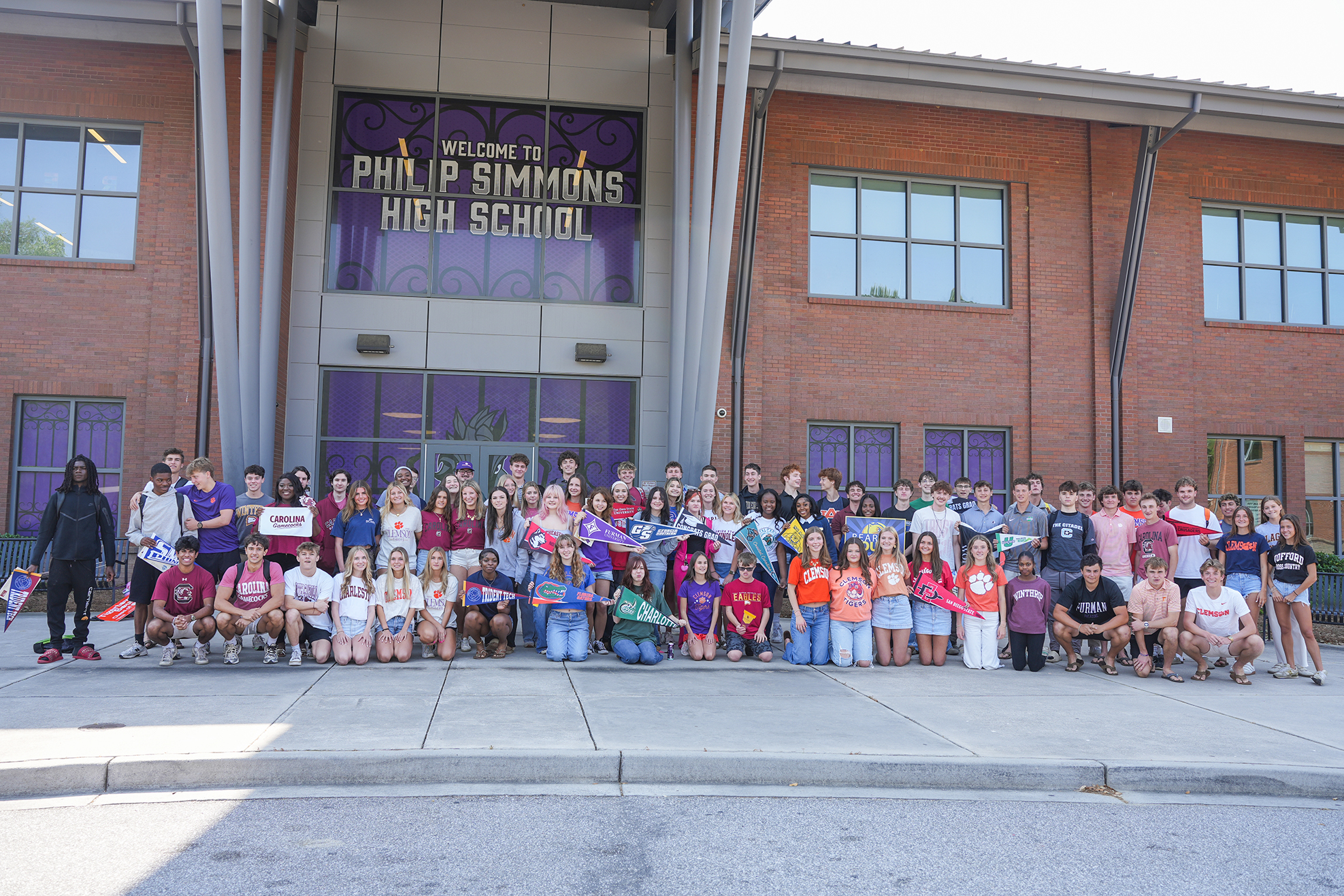 Group of students wearing different colored tops pose for a photo in front of Philip Simmons High School.