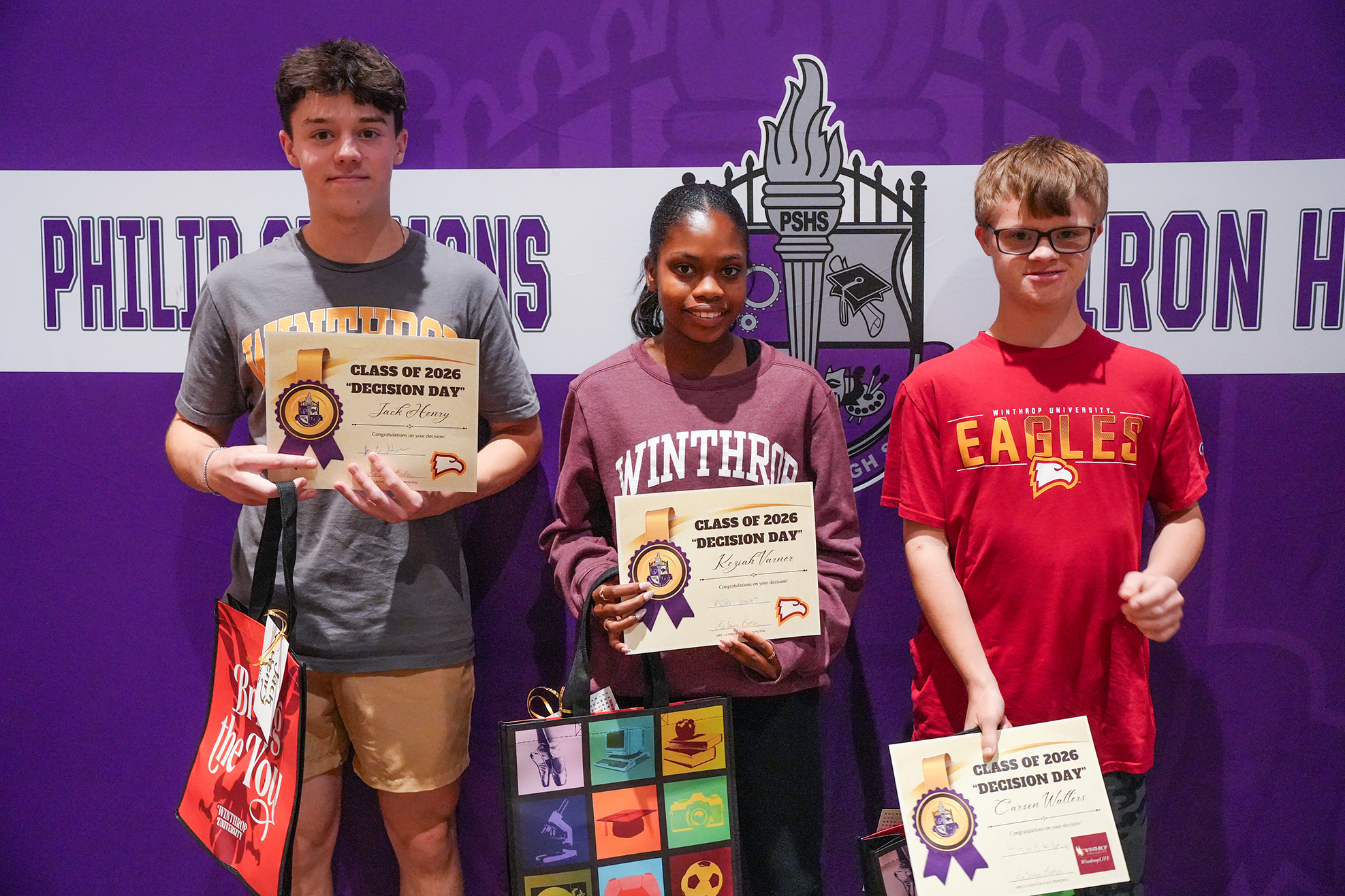 Three students stand against a purple backdrop, each holding certificates. A logo with a torch and letters is in the background.