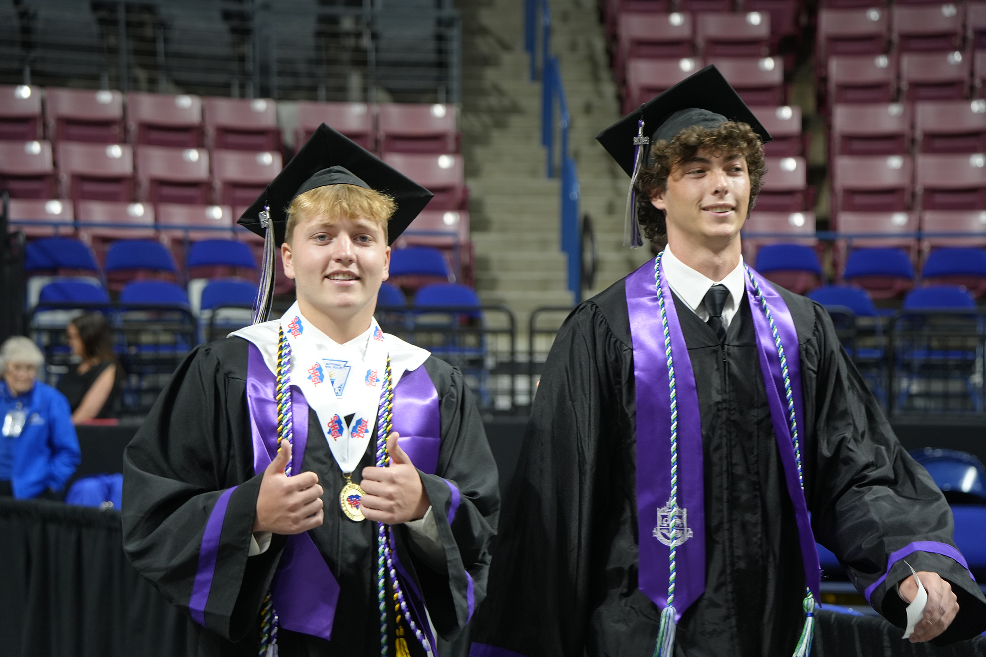 Two men in academic robes and caps stand side by side in an empty auditorium.