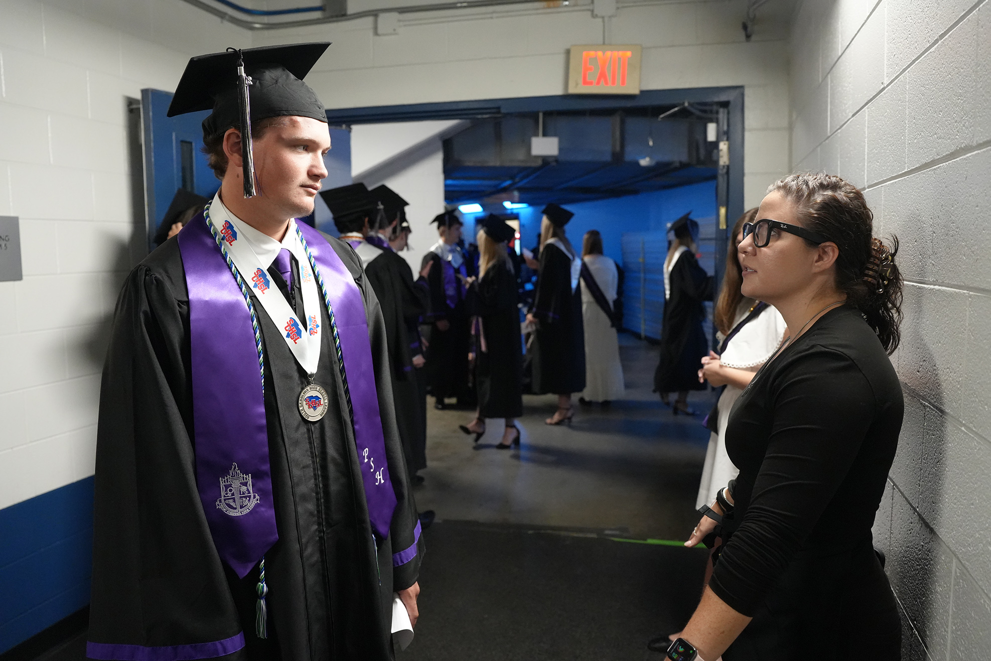 Man in a black cap and gown standing, looking at a woman in front of him.